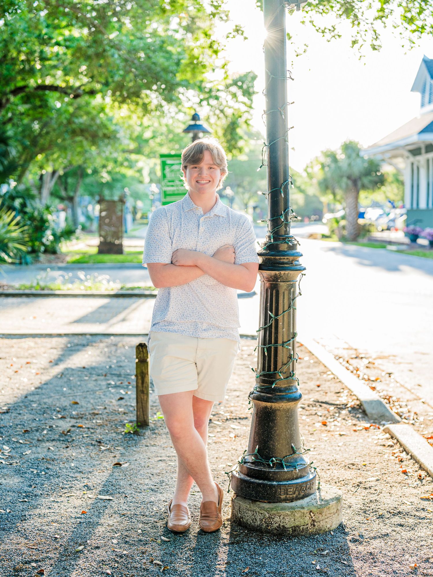 Casual senior photos in white polo near vintage lamp post and tree-lined path.