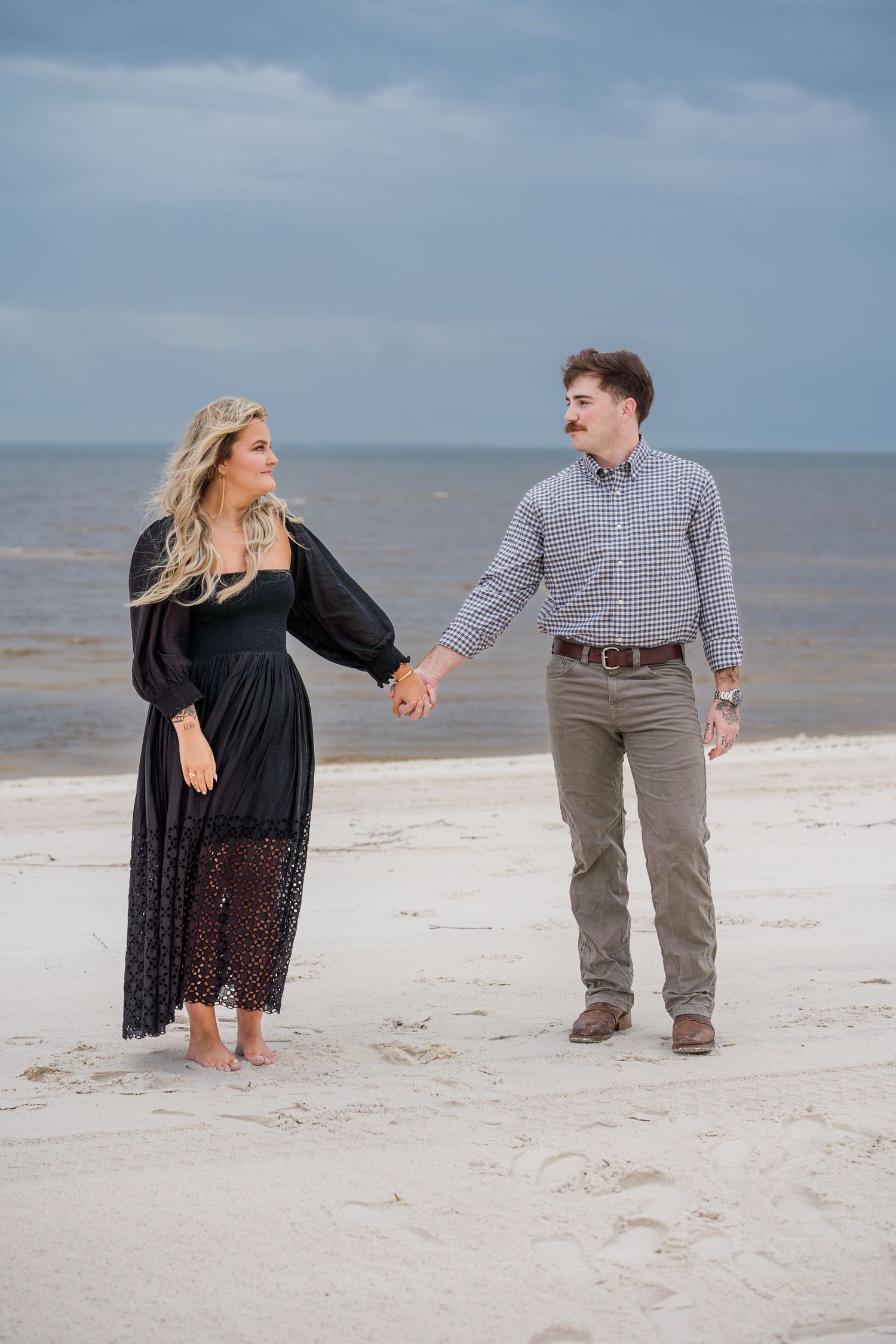 A couple walks hand in hand along a serene beach shoreline.