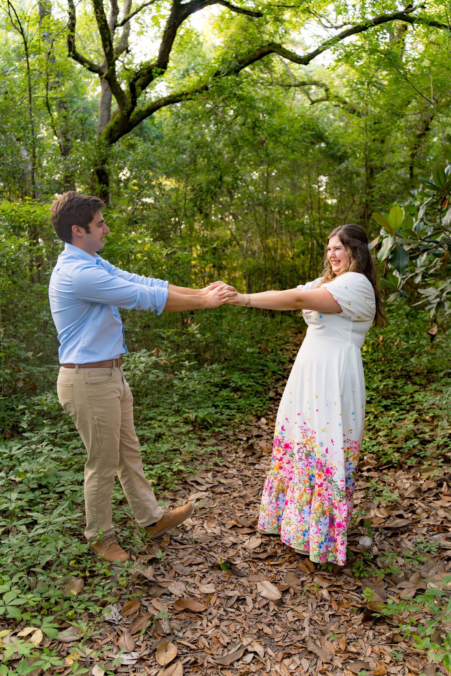 A couple dances playfully in a wooded area during their engagement session.