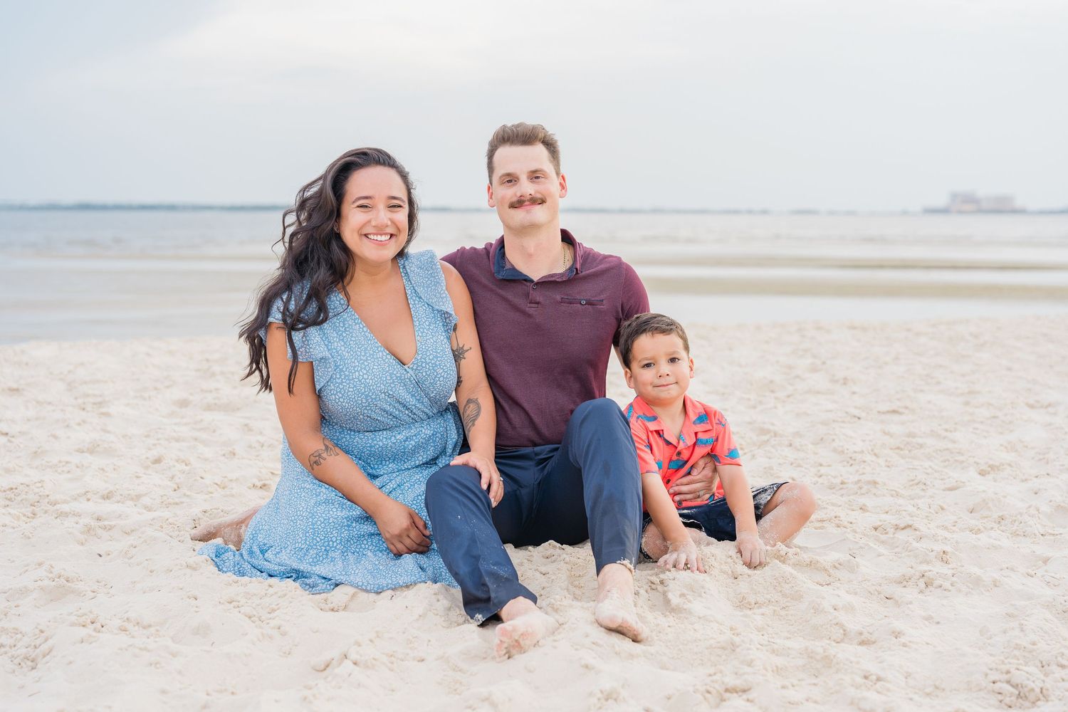 Natural beach portrait of a small family sitting together in the sand.