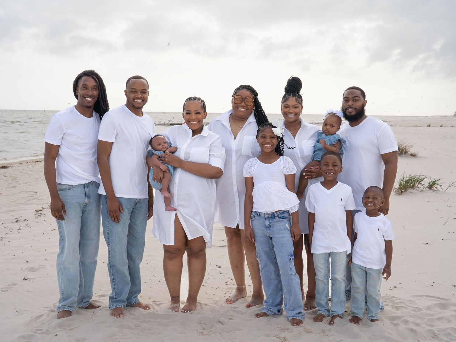 Extended family group photo with coordinated white shirts and jeans on a beach.