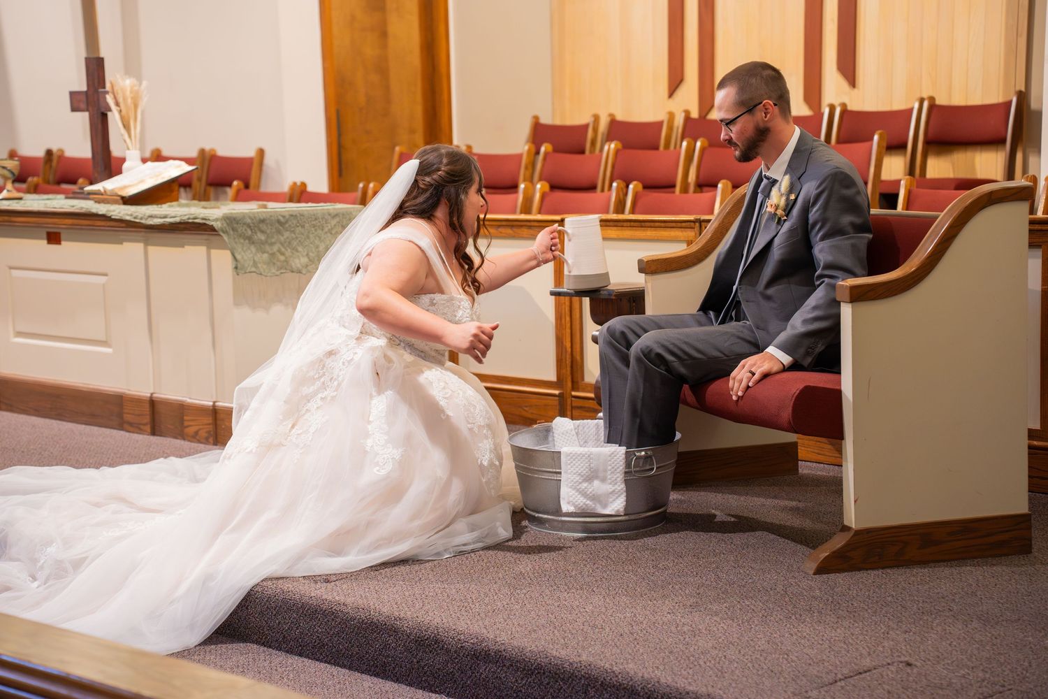 A bride and groom sit together on a church pew while the bride's white dress train flows gracefully across the floor.