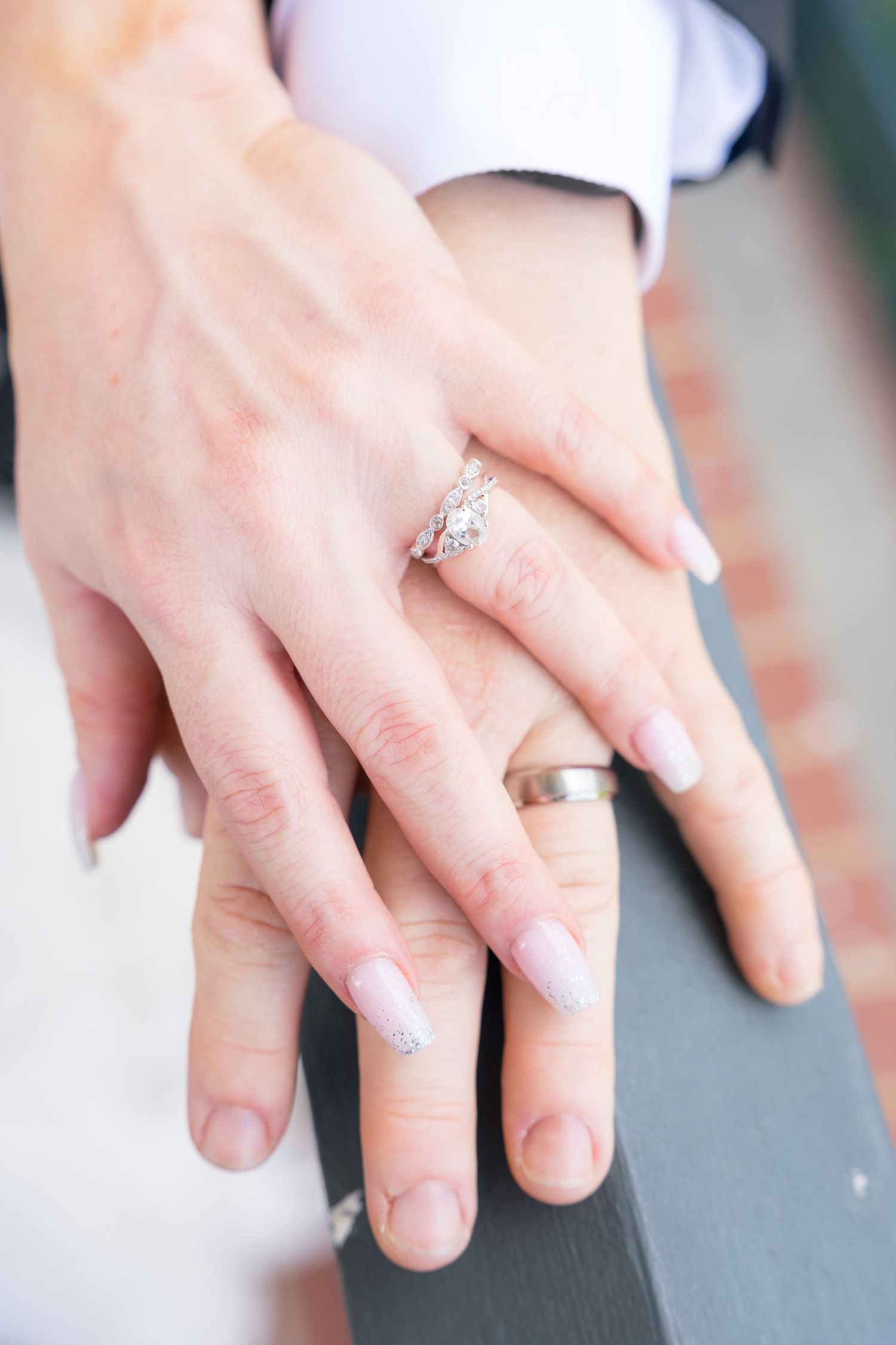 Two hands resting together showing wedding rings, with a diamond engagement ring on the woman's finger.