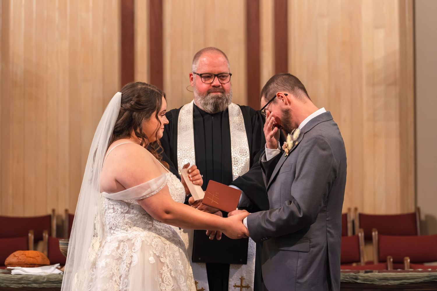 A couple exchanges rings during their wedding ceremony in a church with an officiant presiding over the service.