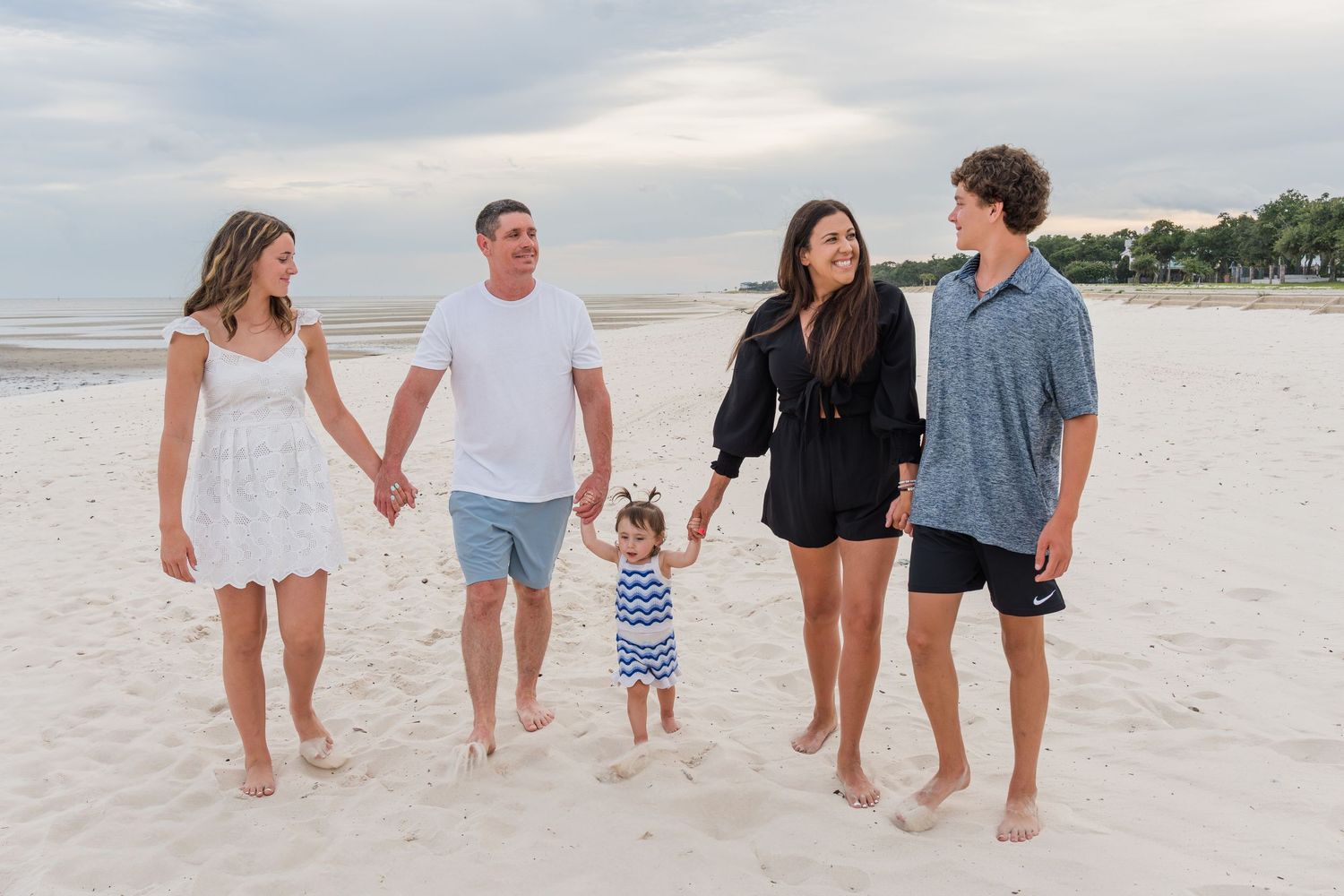 Extended family group poses casually while walking along a beach at dusk.