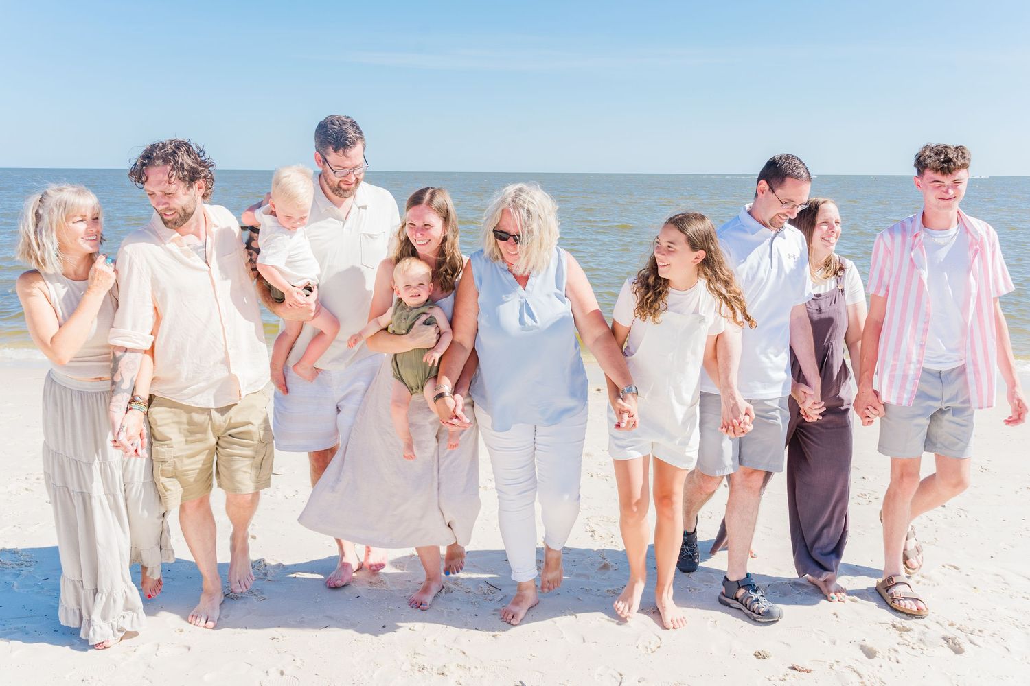 Large group in coordinated white and beige outfits poses for a casual beach photo.
