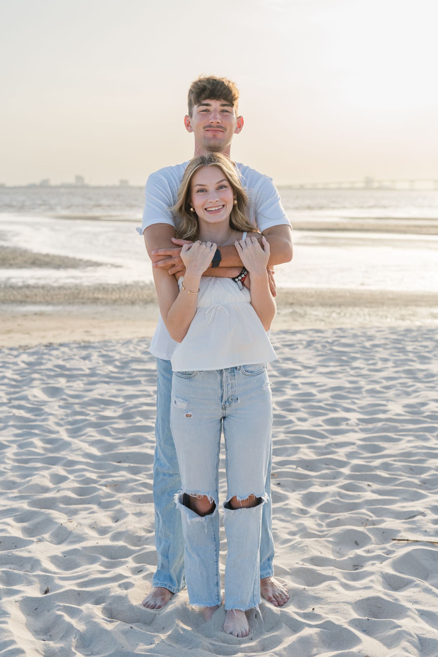 Couple shares a playful moment while posing on the beach at sunset.