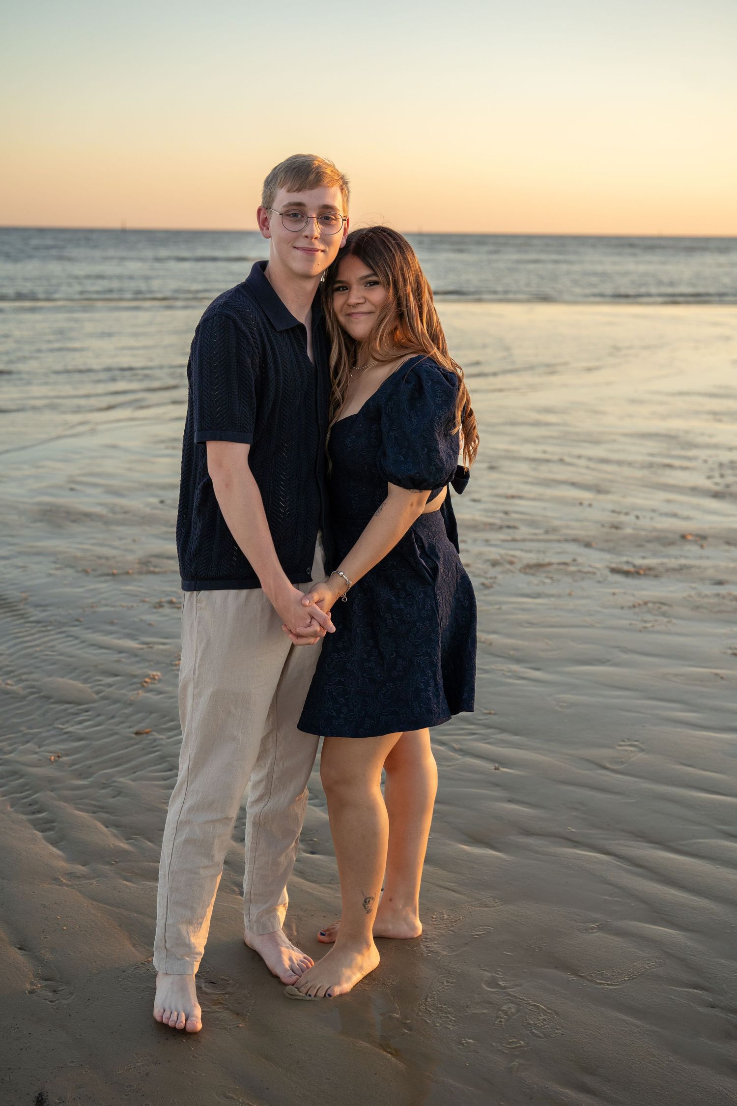 A couple shares an intimate moment while walking barefoot on the beach at sunset.