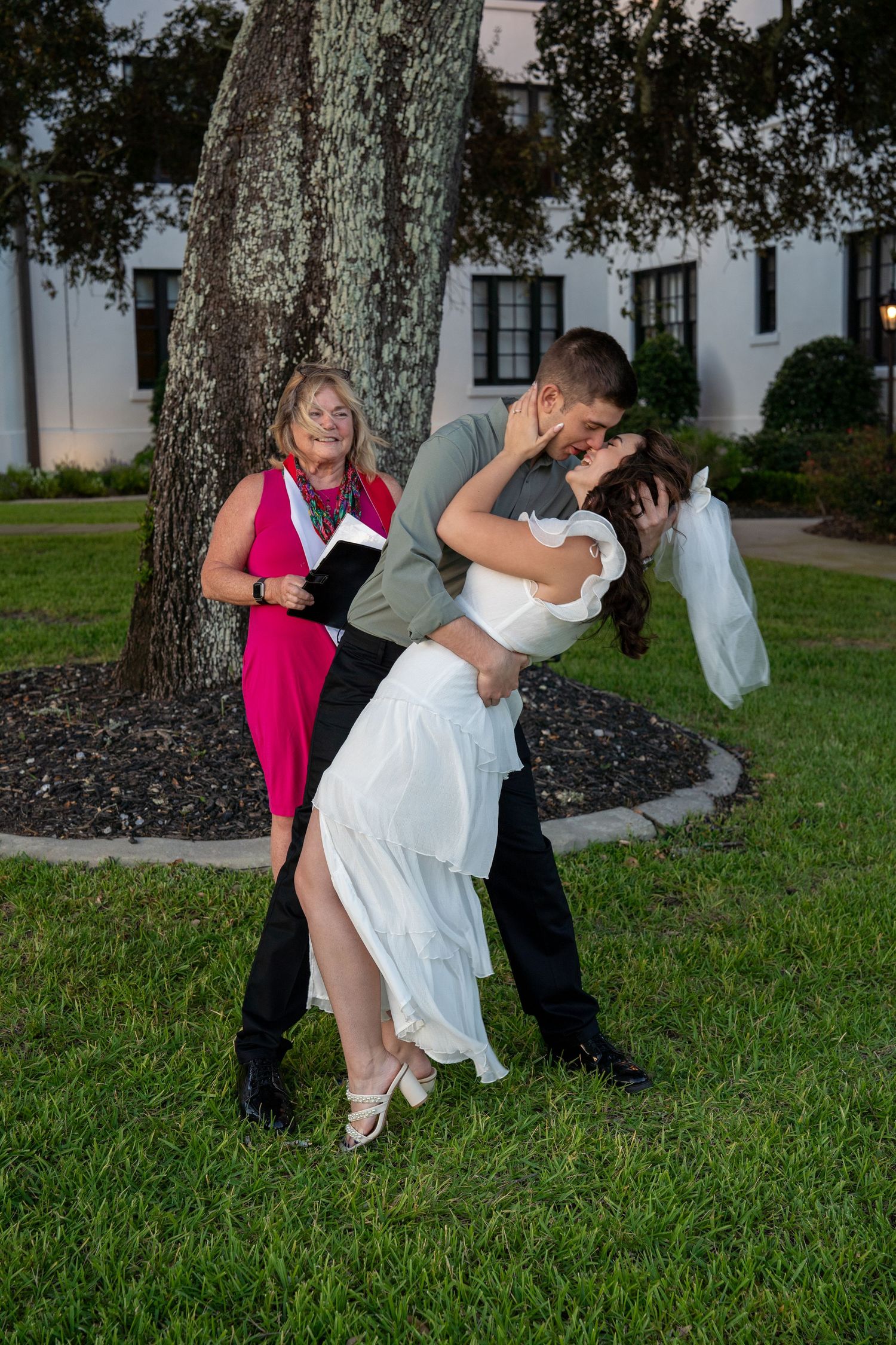Playful wedding party photos being taken under large oak trees on a grassy lawn.