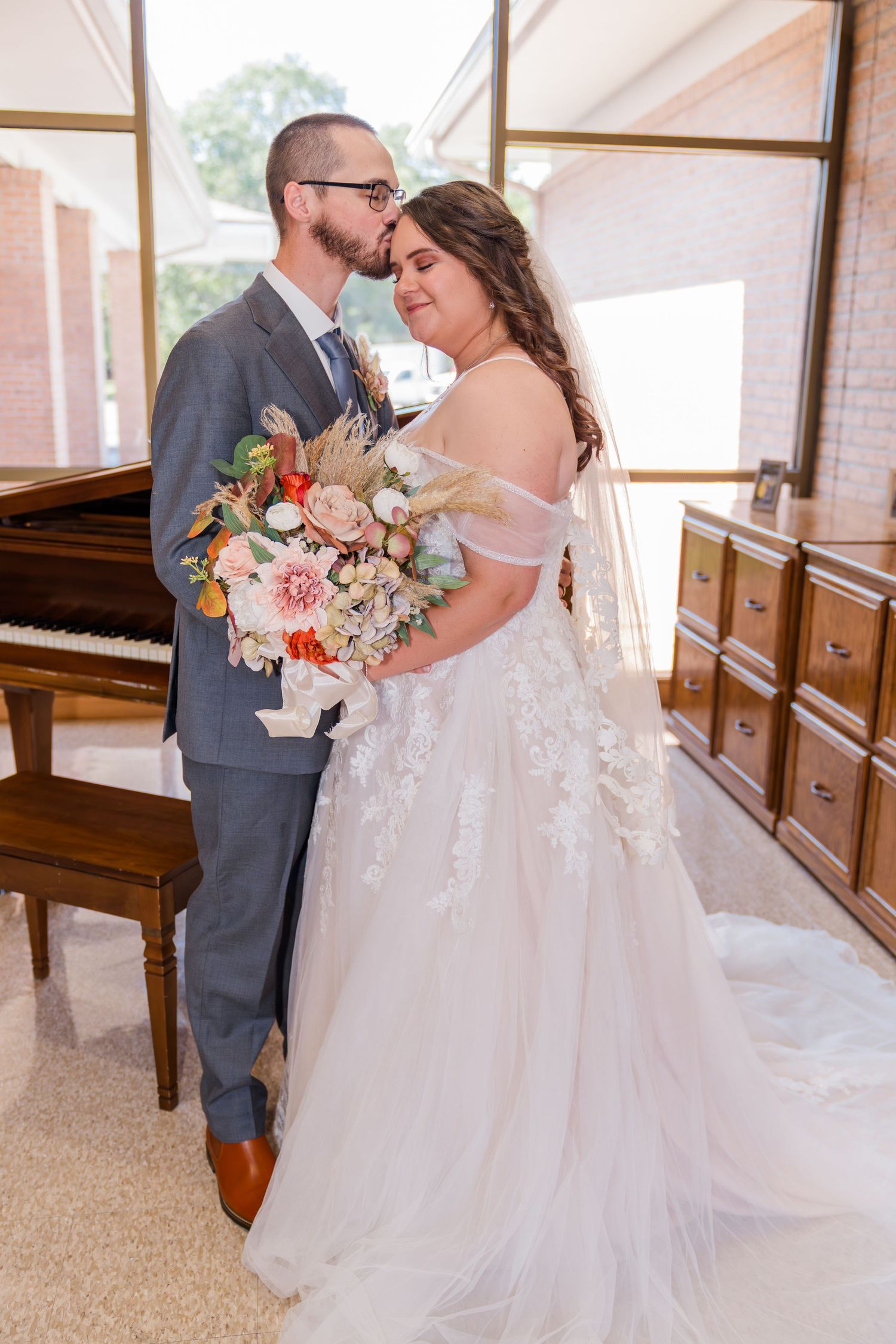 A romantic wedding moment with a couple embracing by a piano, featuring a beautiful floral bouquet and flowing white gown.