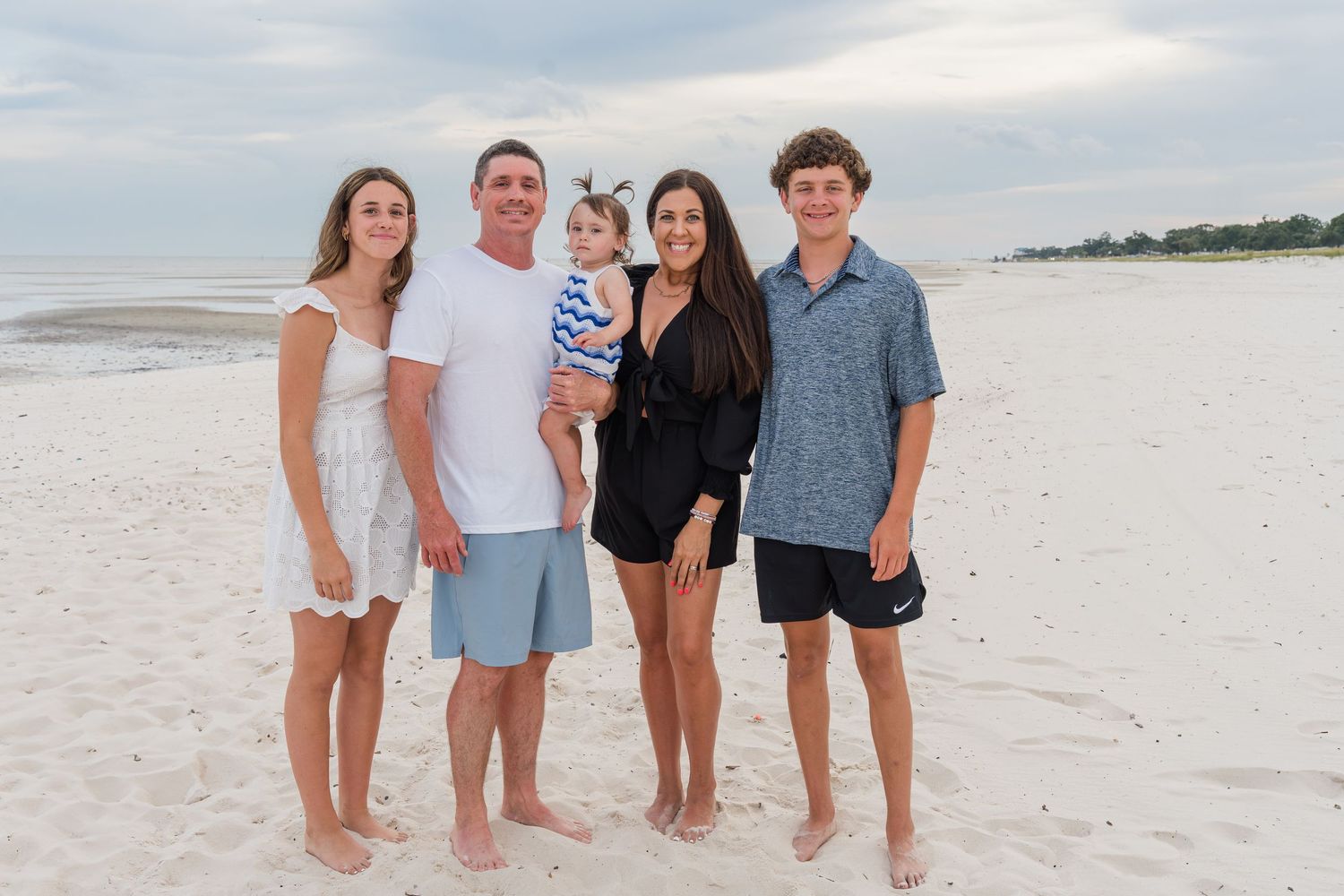 Family walking together on pristine white sand beach during sunset photo session.