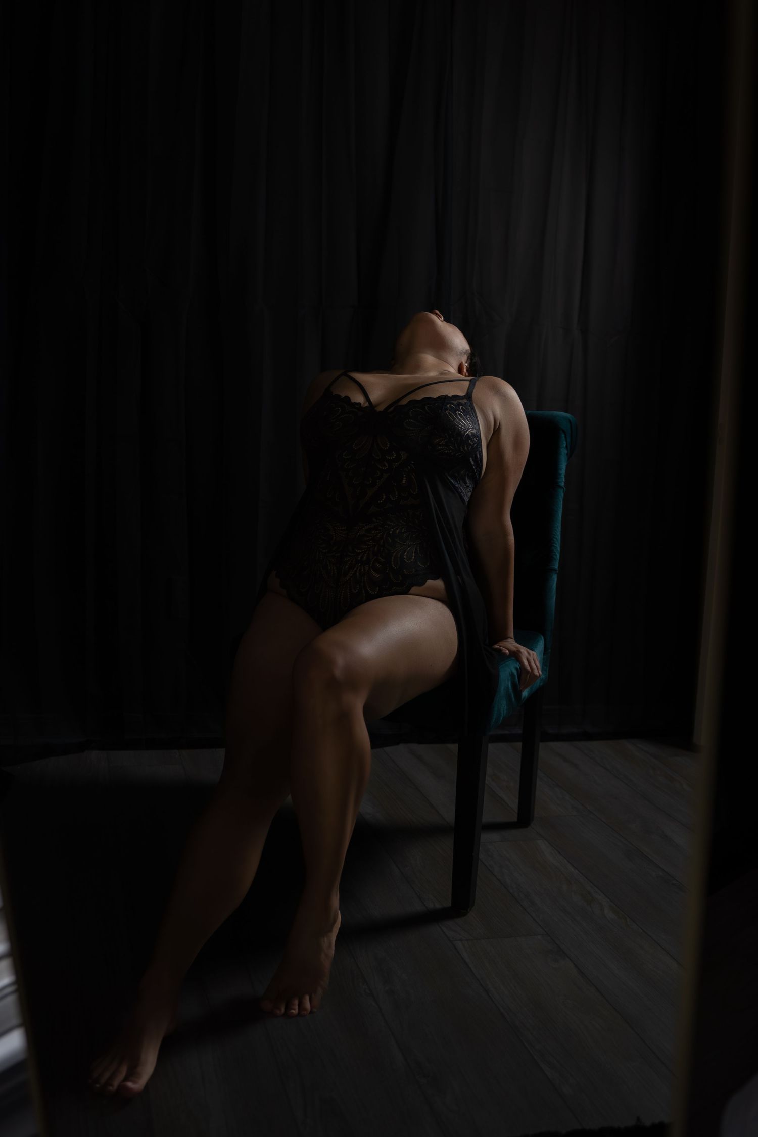 Moody portrait of person in black bodysuit posing on chair against dark background.