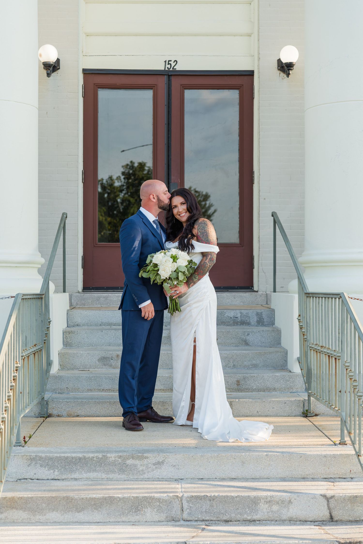 An elegant couple poses on white stone steps of a historic building.