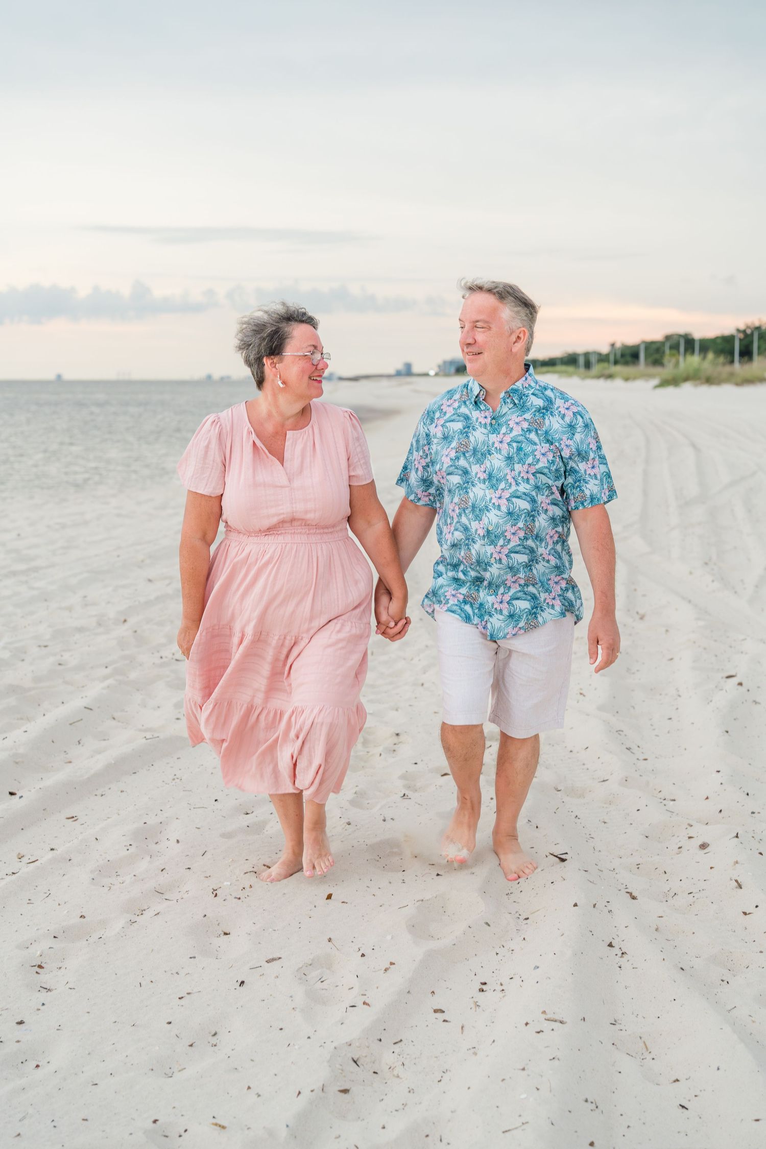Two people in colorful outfits walking together on a white sandy beach.