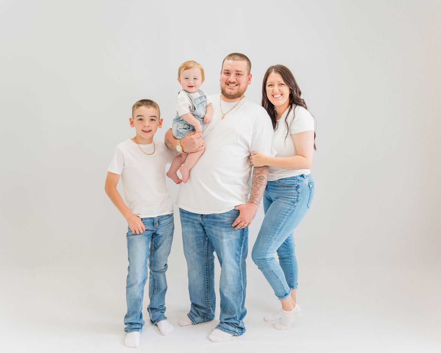 Family wearing casual white and denim outfits posing against white background.