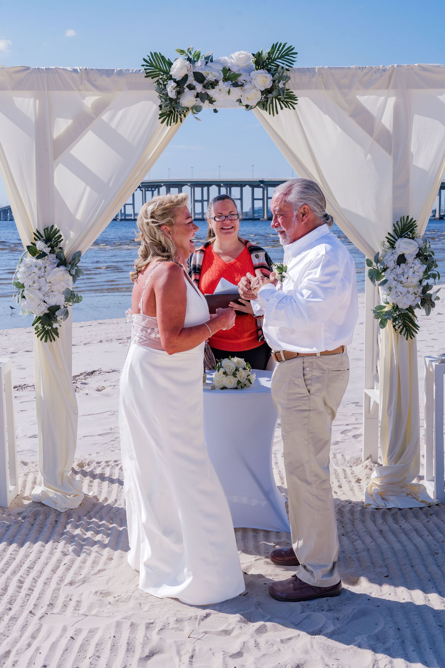 A beach wedding ceremony sequence showing decorative white fabric draped gazebos and floral arrangements on a sandy shore.