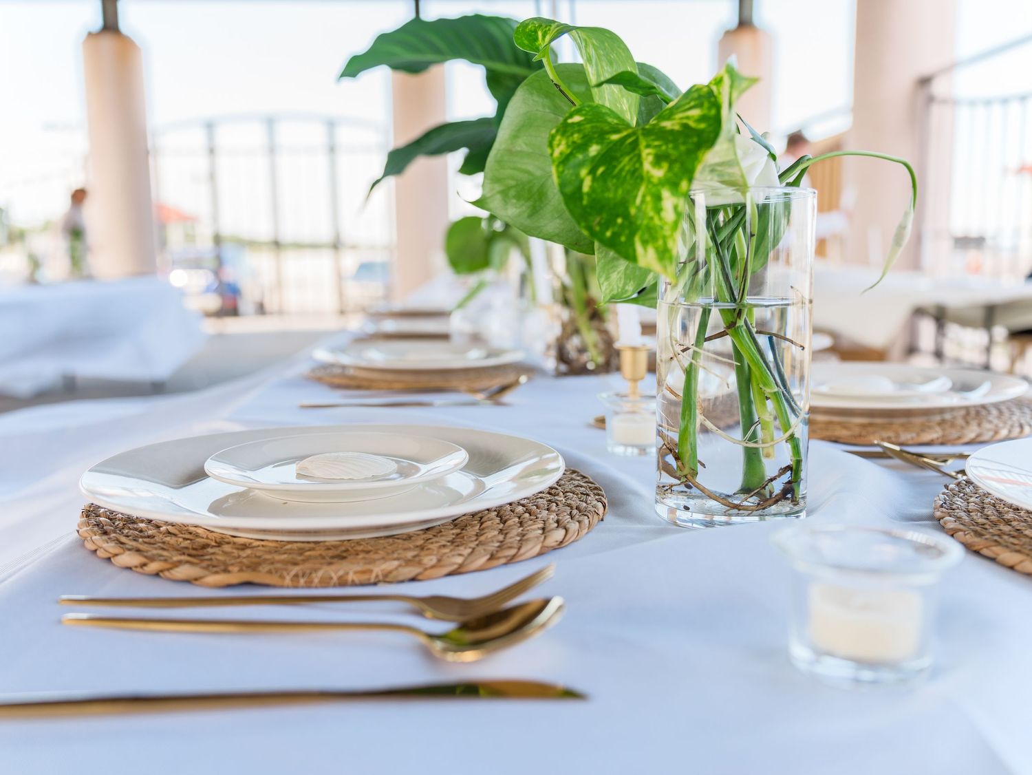 Elegant table setting with white linens, woven placemats and fresh greenery centerpieces.