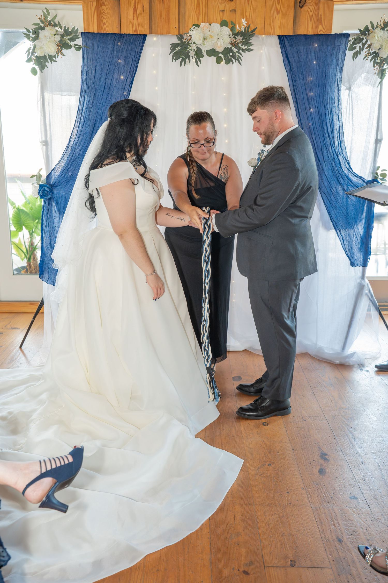 Indoor wedding ceremony with blue drapery and greenery decorations.