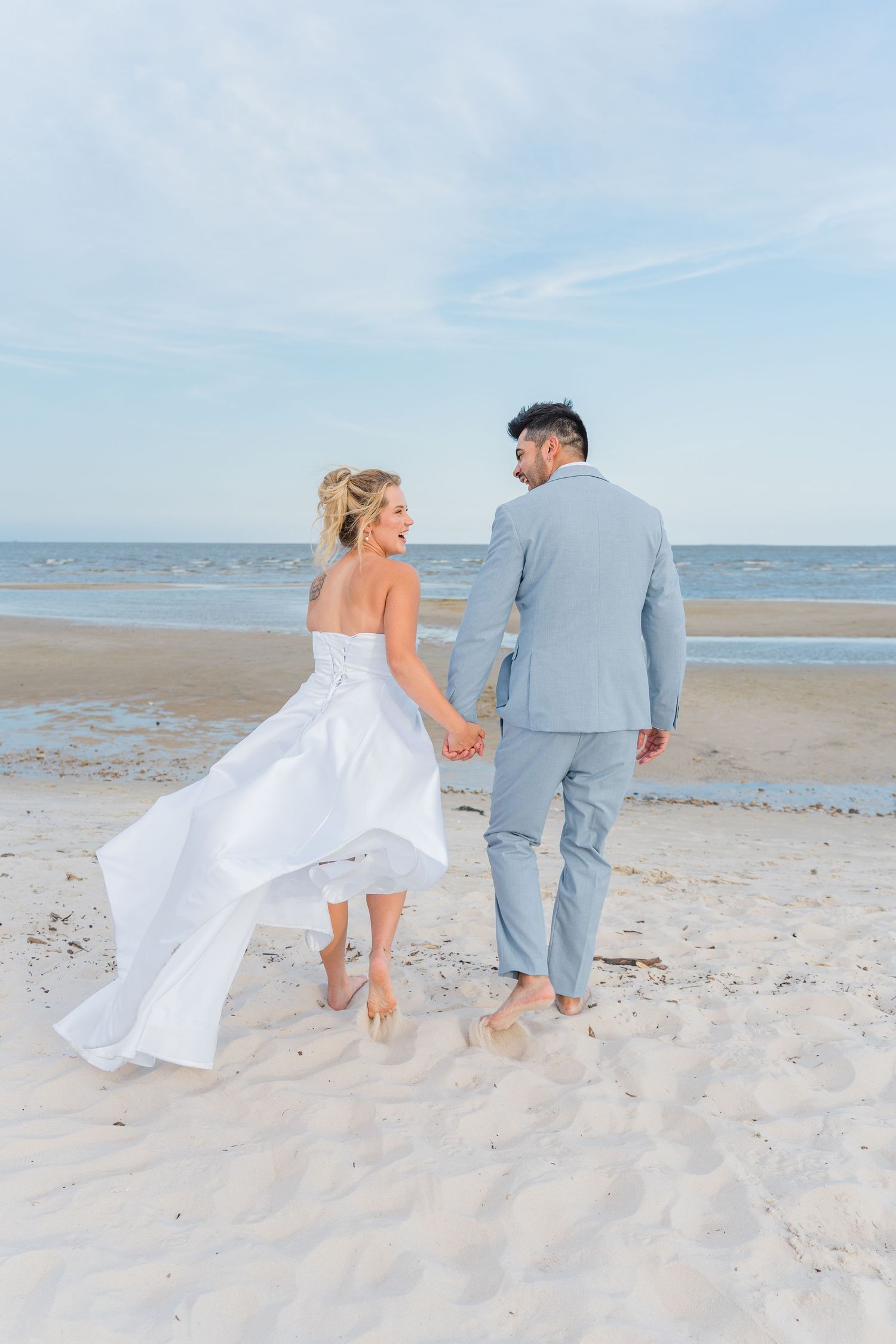 Romantic beach wedding photoshoot showing couple walking along white sandy shore.