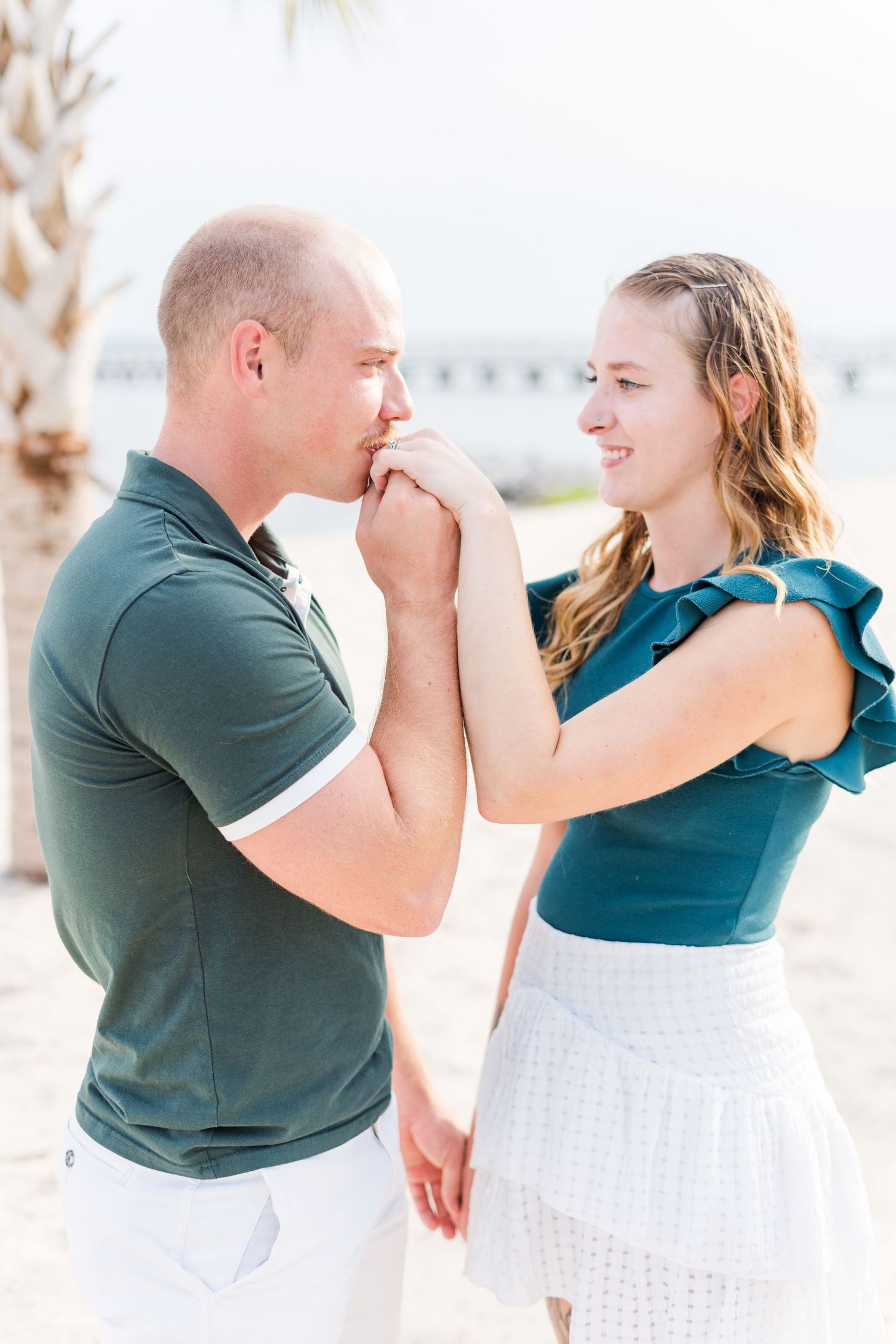 A playful couple in teal and white outfits share tender moments on the beach.