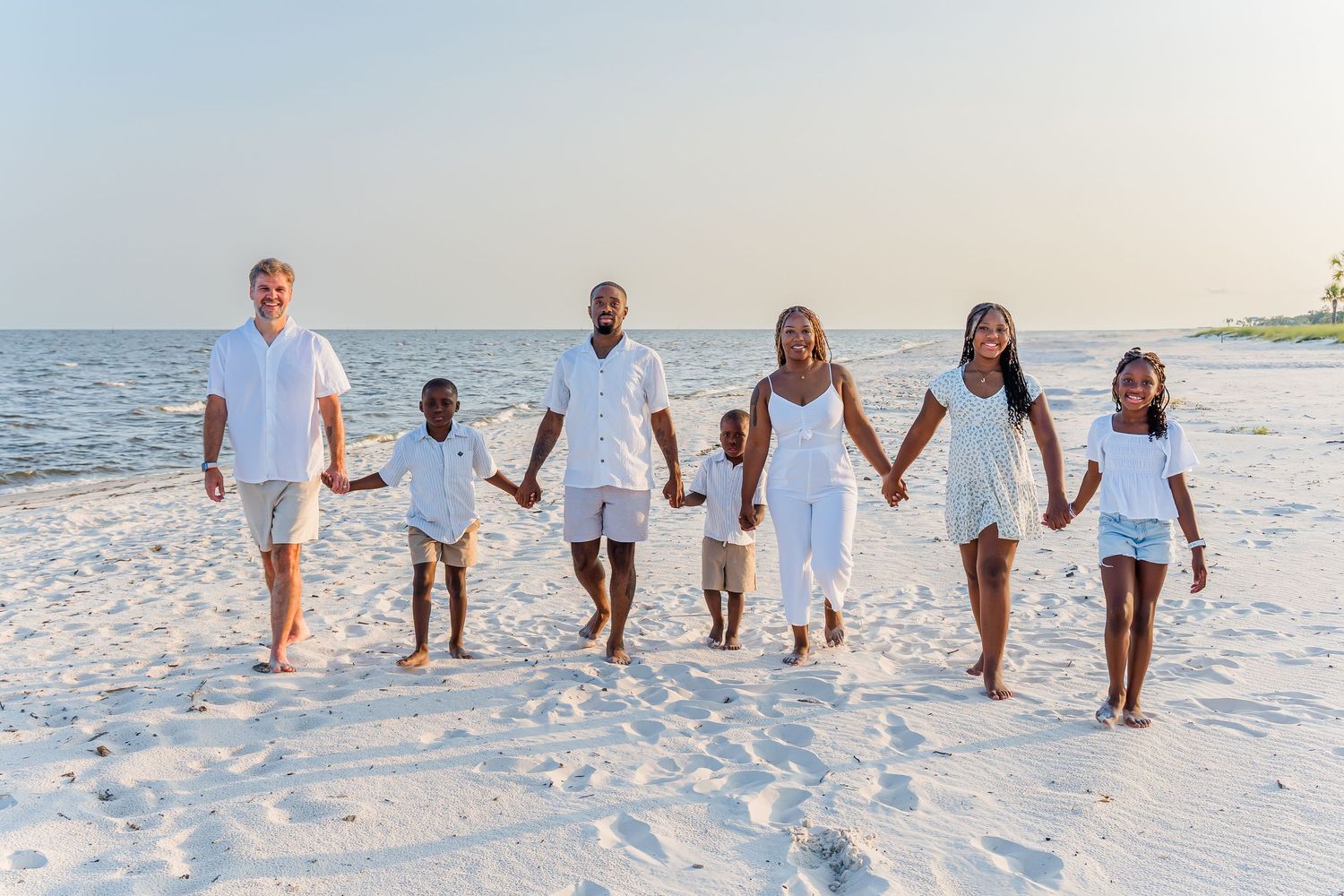 Beach portrait session with group arranged in staggered poses on white sand.