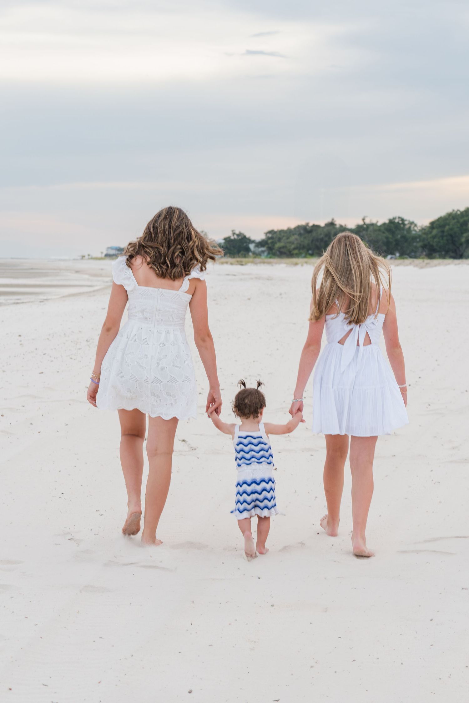 Family walking along white sandy beach wearing matching white dresses.