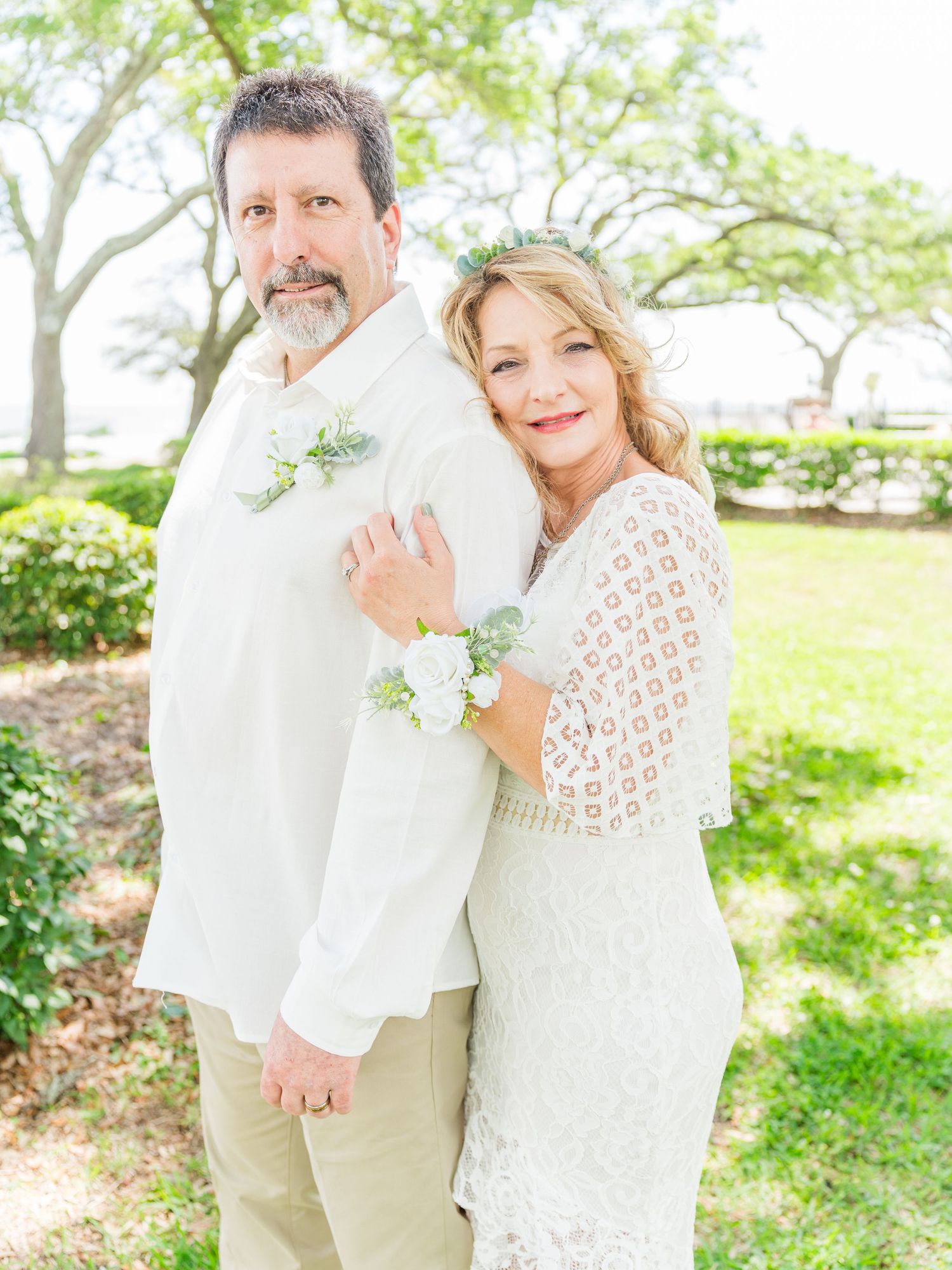 A romantic outdoor wedding portrait with white lace and casual attire in a lush green setting.