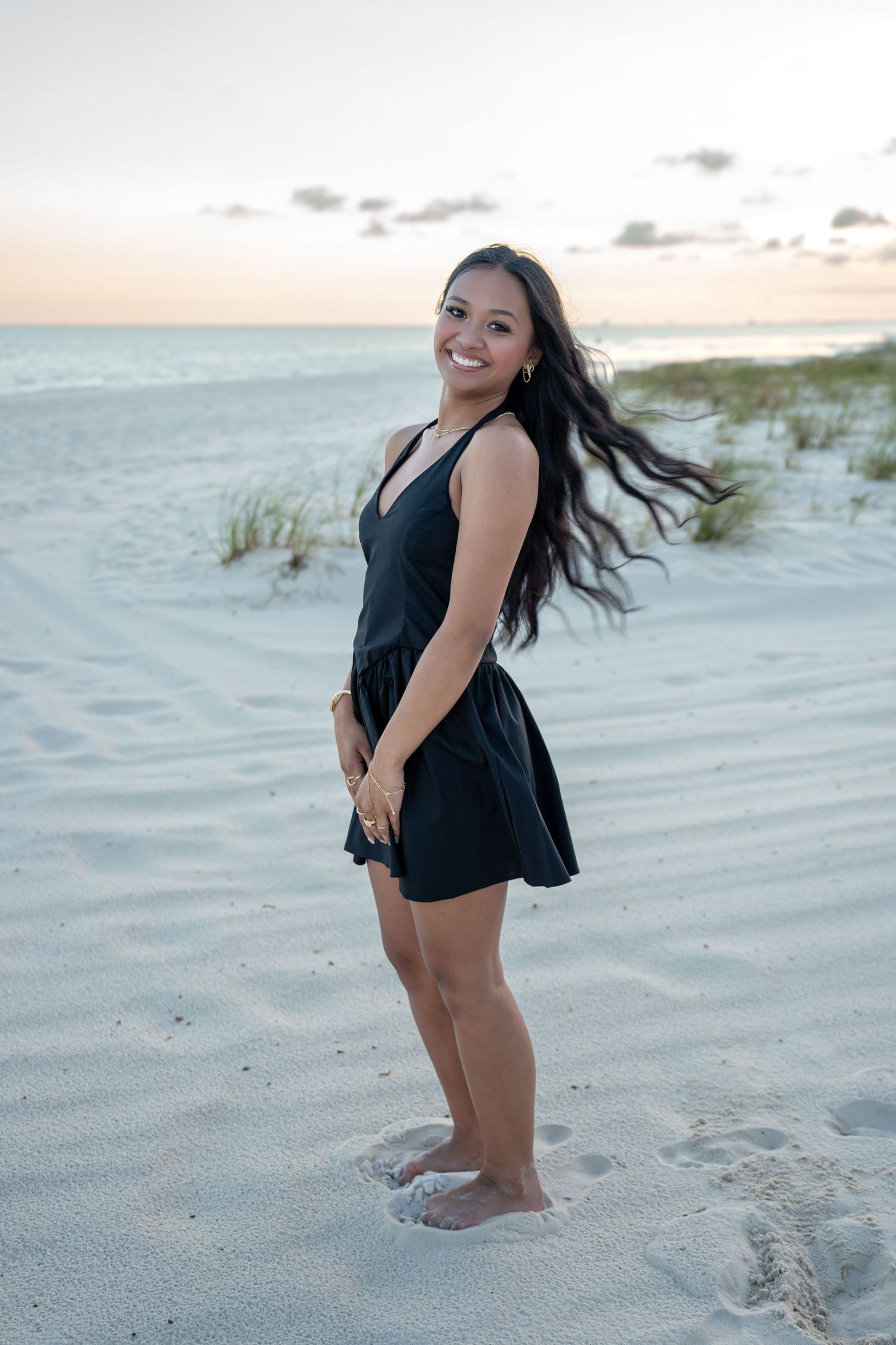 Playful beach photoshoot at sunset with black dress on white sand.