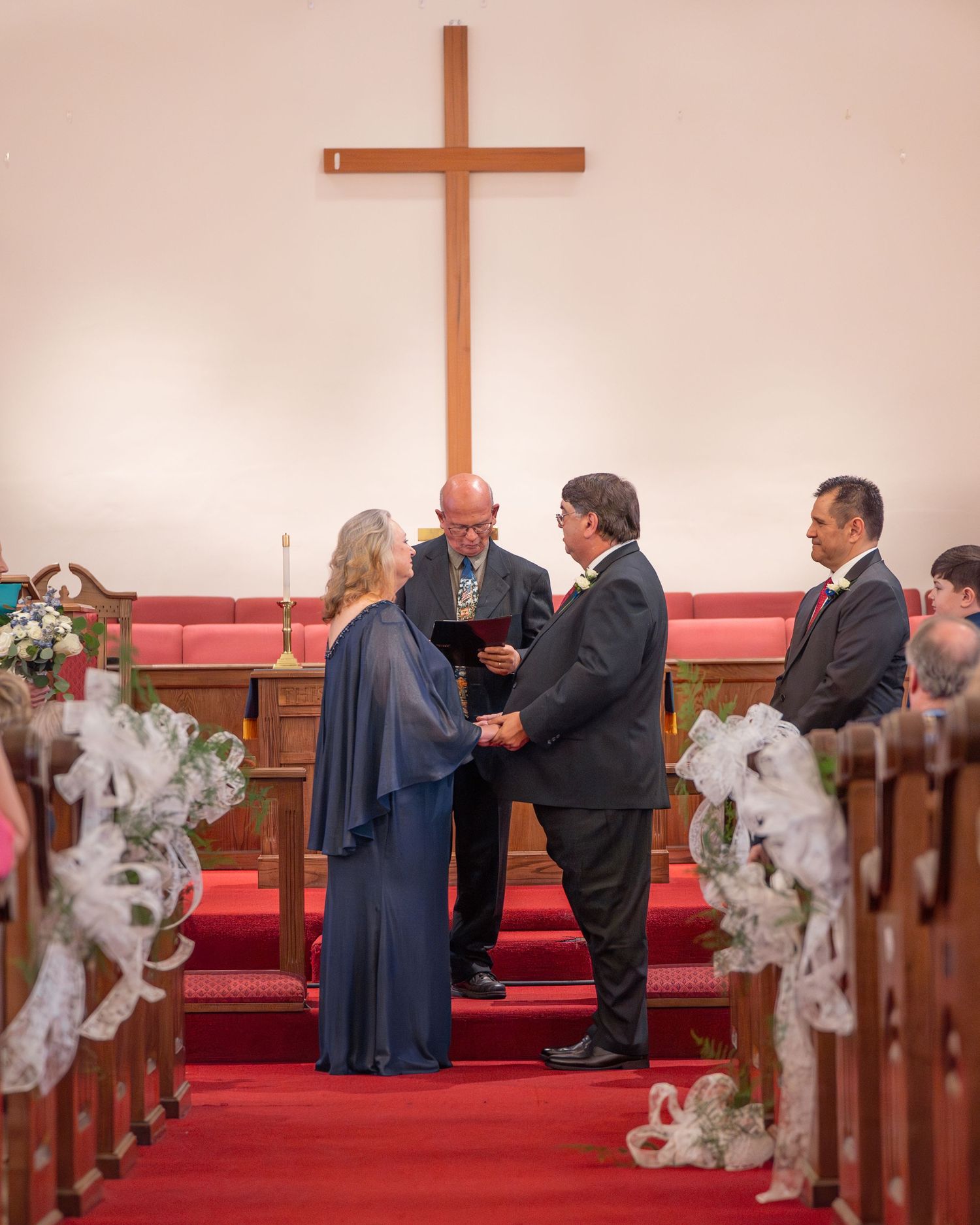 A traditional church wedding ceremony with wooden pews and a prominent cross on the altar wall.