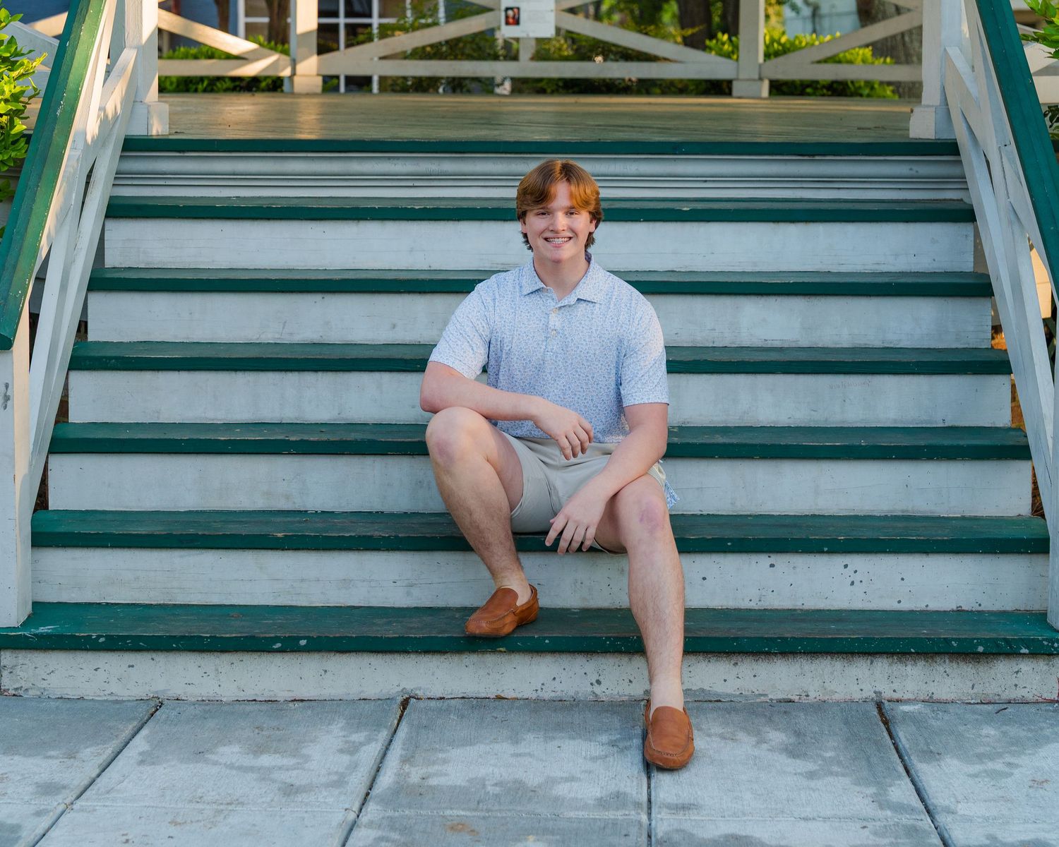 Person sitting on green wooden outdoor steps in casual summer attire.