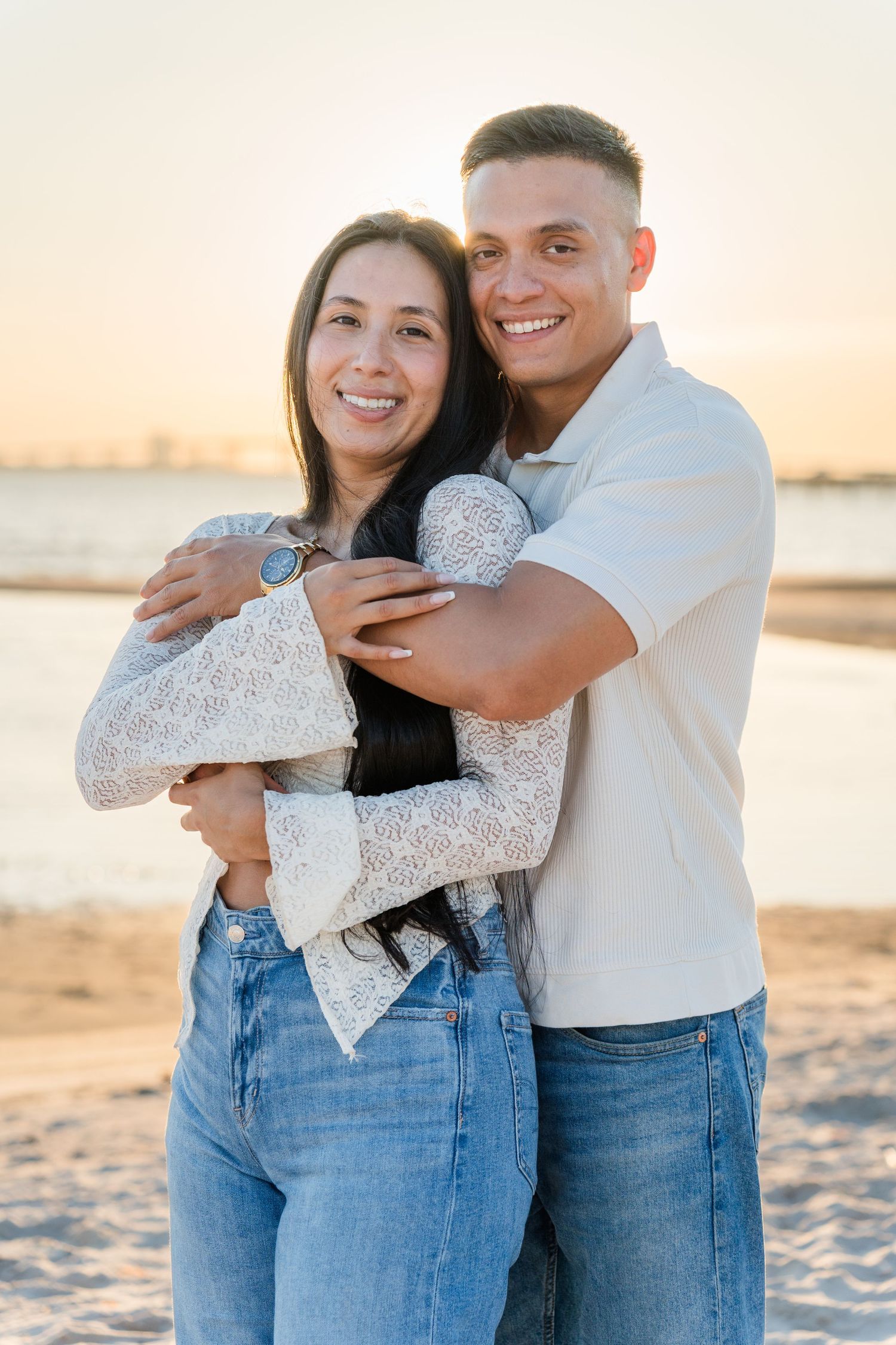 A couple embraces on a sandy beach at sunset wearing matching white and denim outfits.