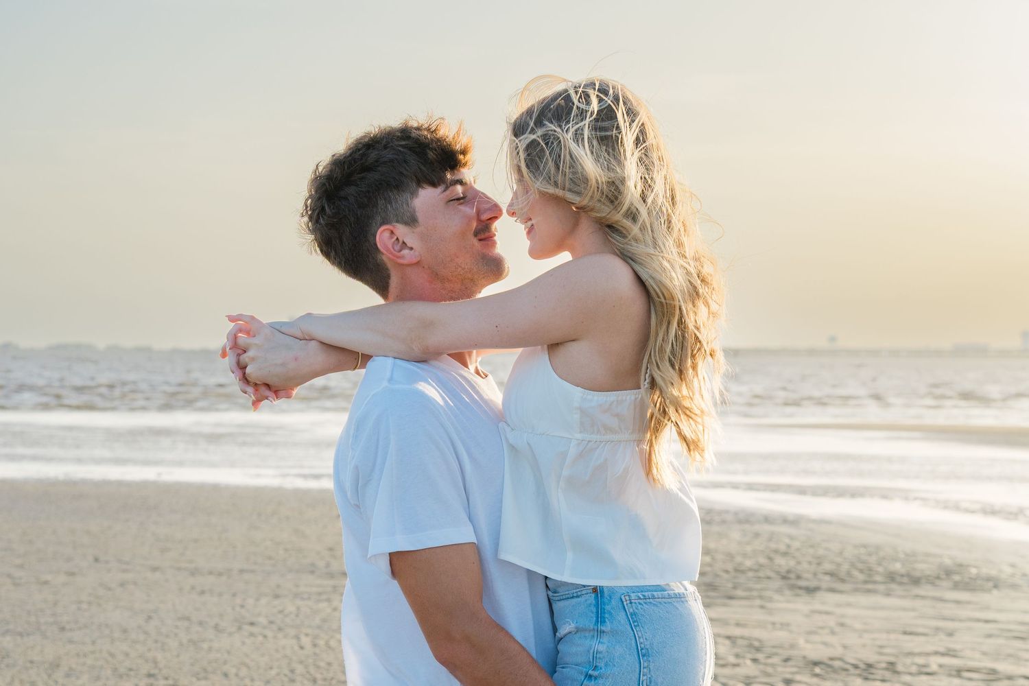Couple embracing on sandy beach during golden hour with waves crashing behind them.