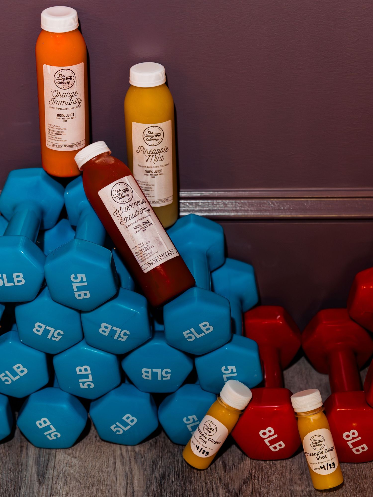 Colorful juice bottles displayed against blue and red exercise weights in a fitness setting.