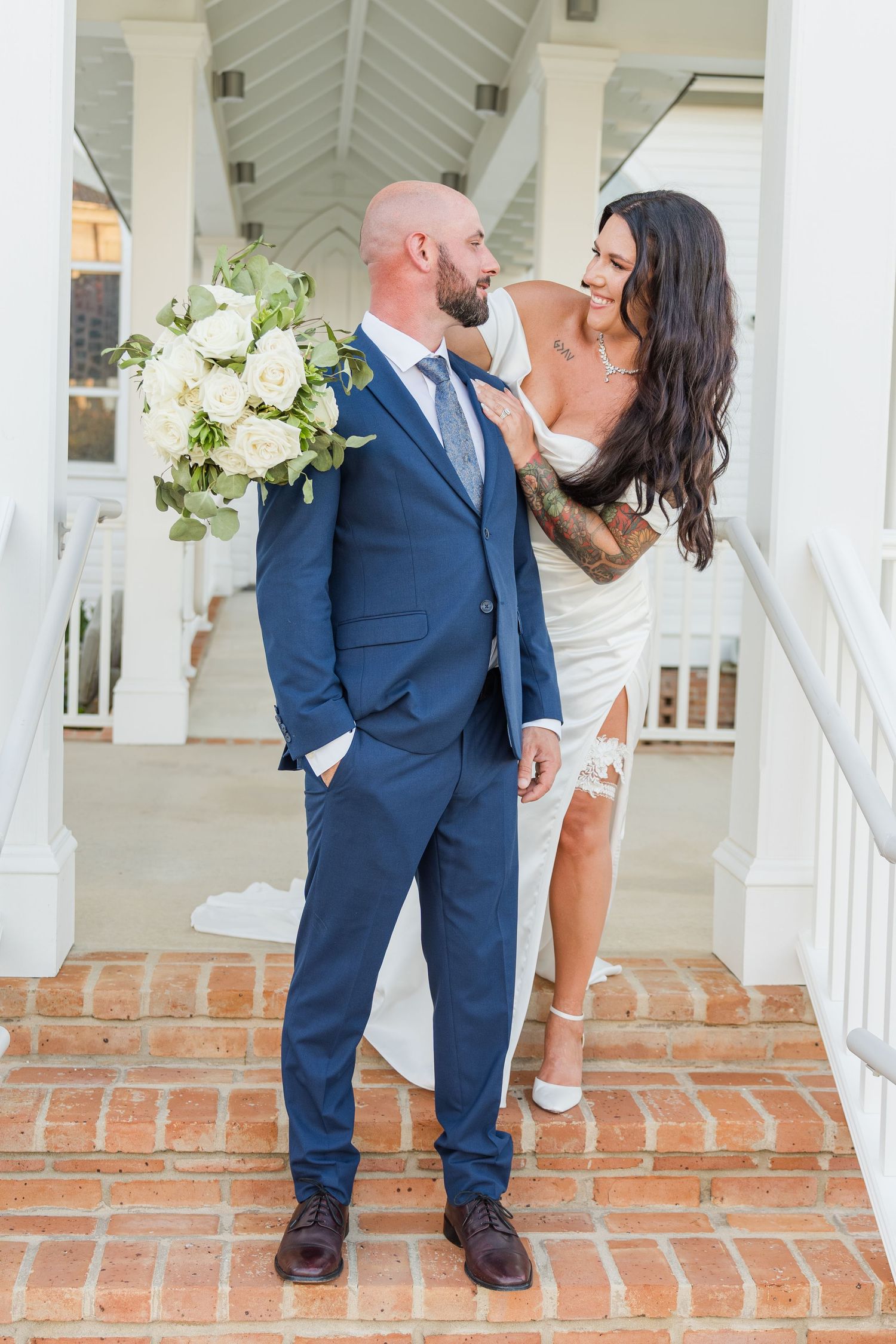 Bride in white dress and groom in navy suit share romantic poses beneath white columns.