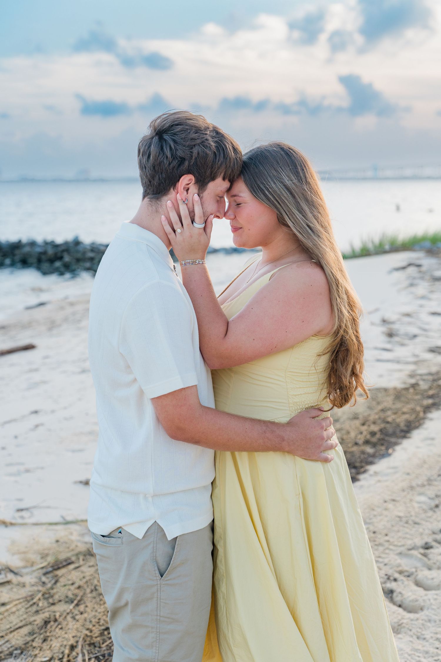 Couple sharing a romantic moment on a sandy beach at sunset, woman in yellow dress, man in white shirt.
