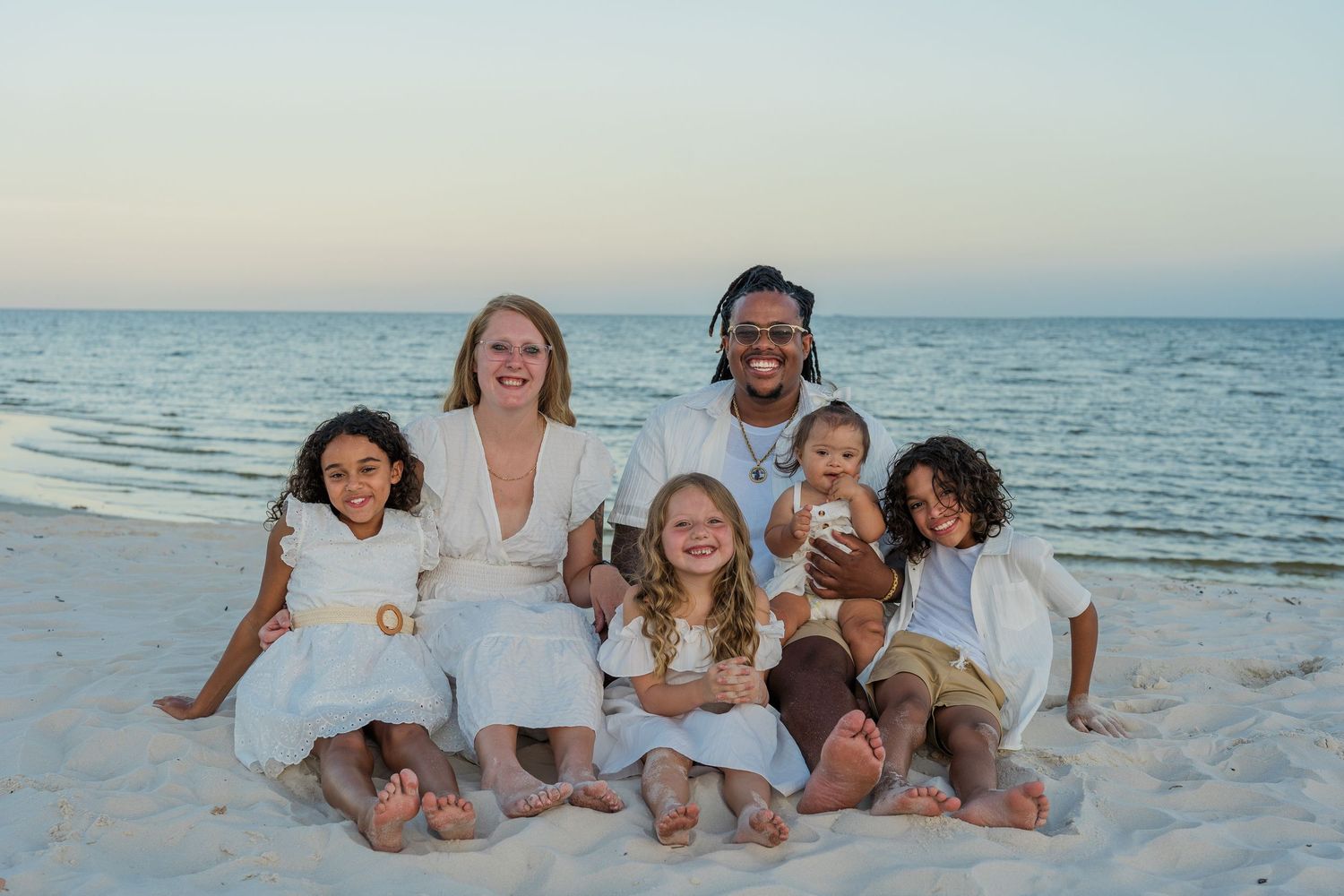 Family sitting together on white sand beach at sunset.