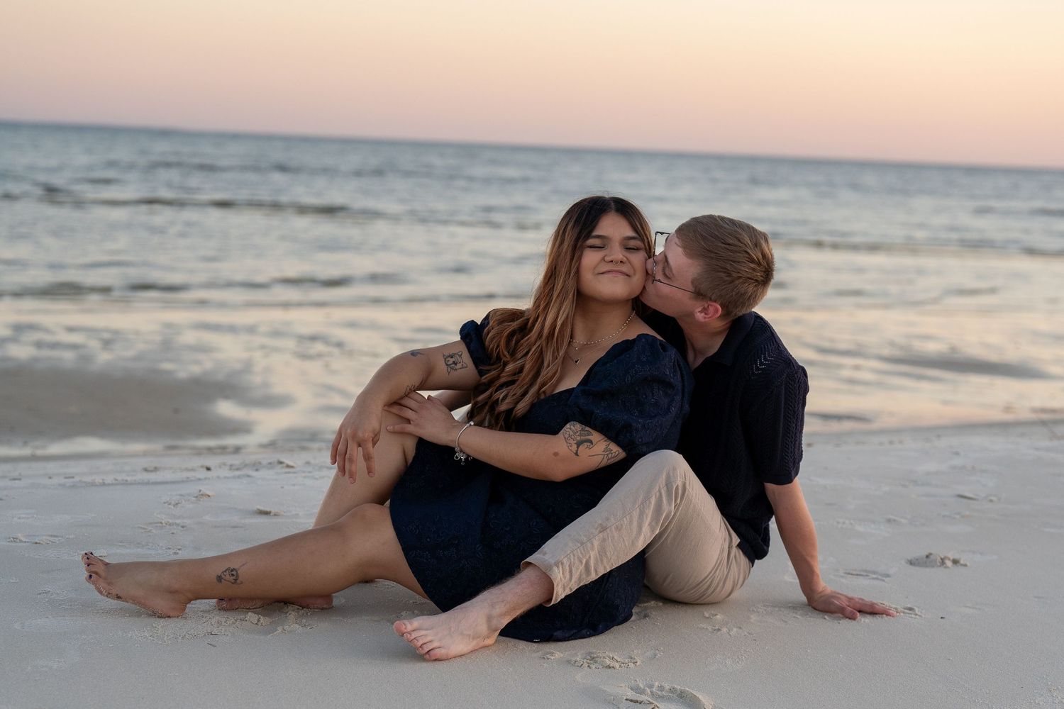 A couple enjoys a romantic moment lying on the beach sand during sunset.