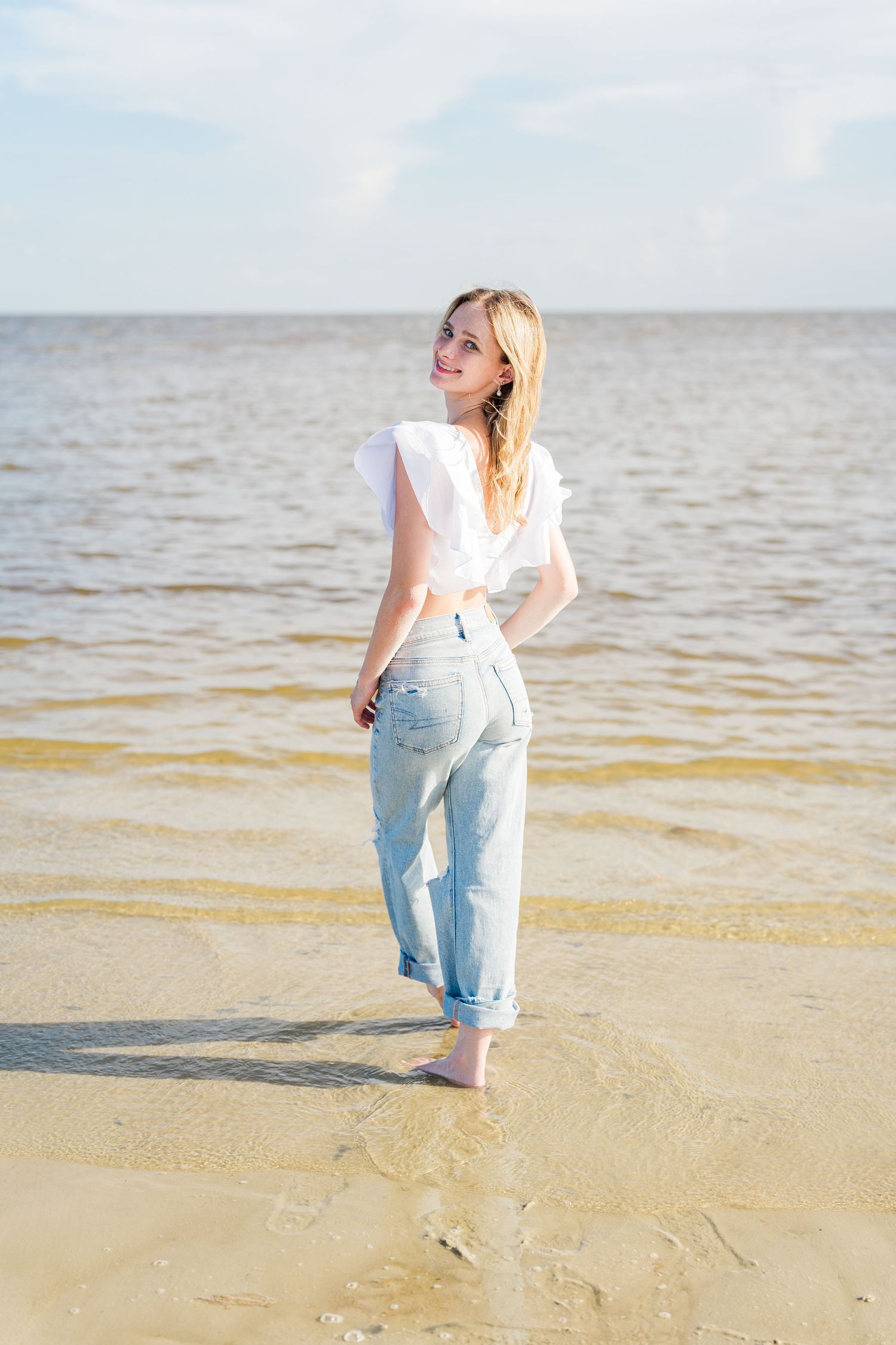 A figure in white and denim walks along the shoreline at sunset.