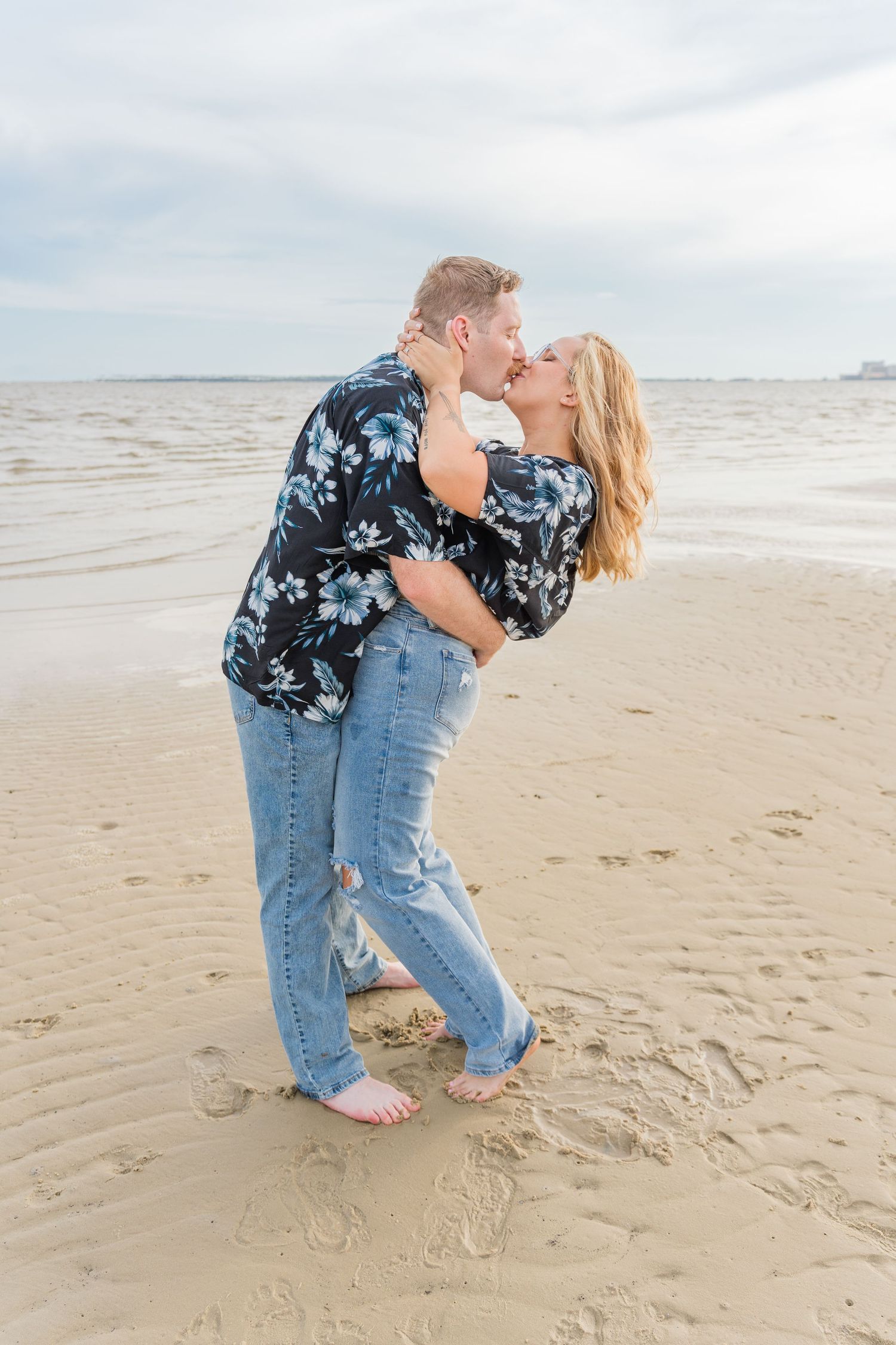 A romantic couple shares intimate moments on a beach in casual attire.