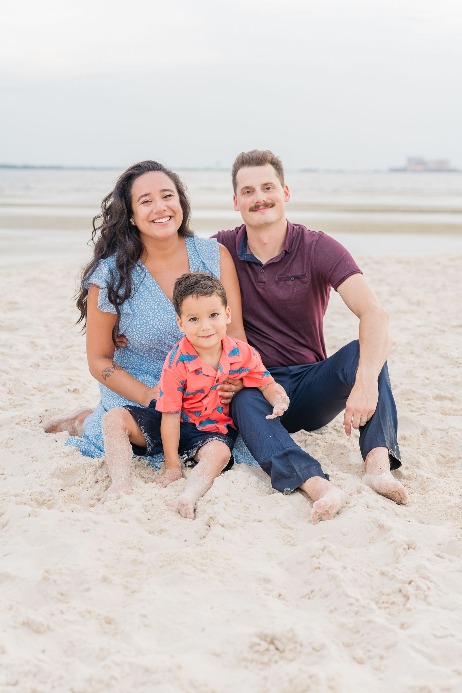 Family sitting together on sandy beach during sunset photo session.