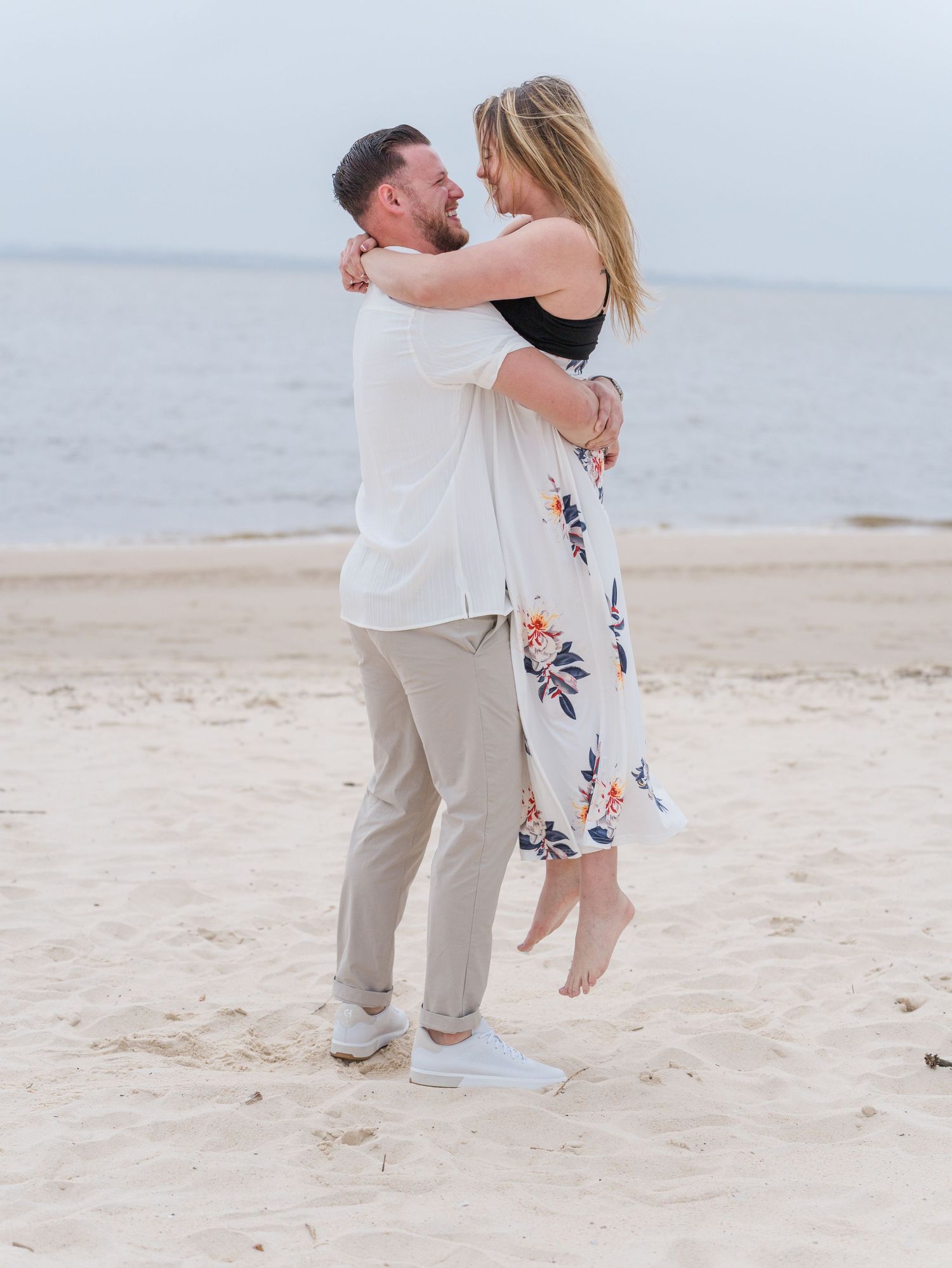A couple celebrates their engagement with romantic poses on a sunny beach.