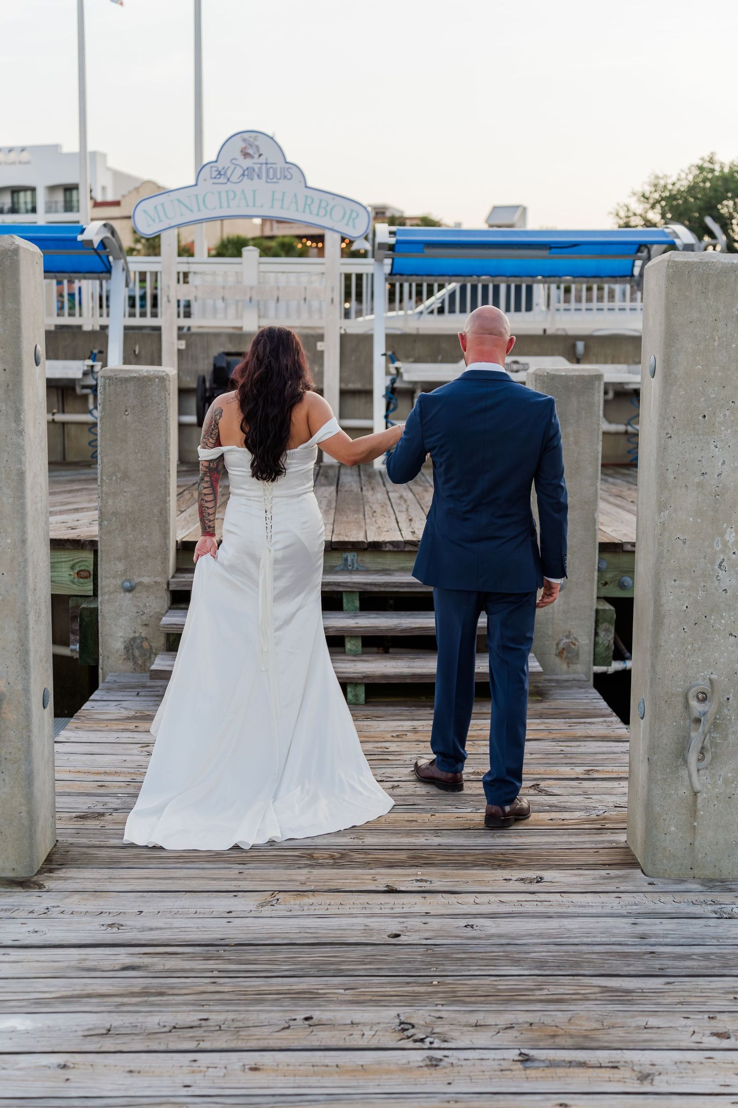 Wedding couple and guests standing on wooden pier overlooking marina.