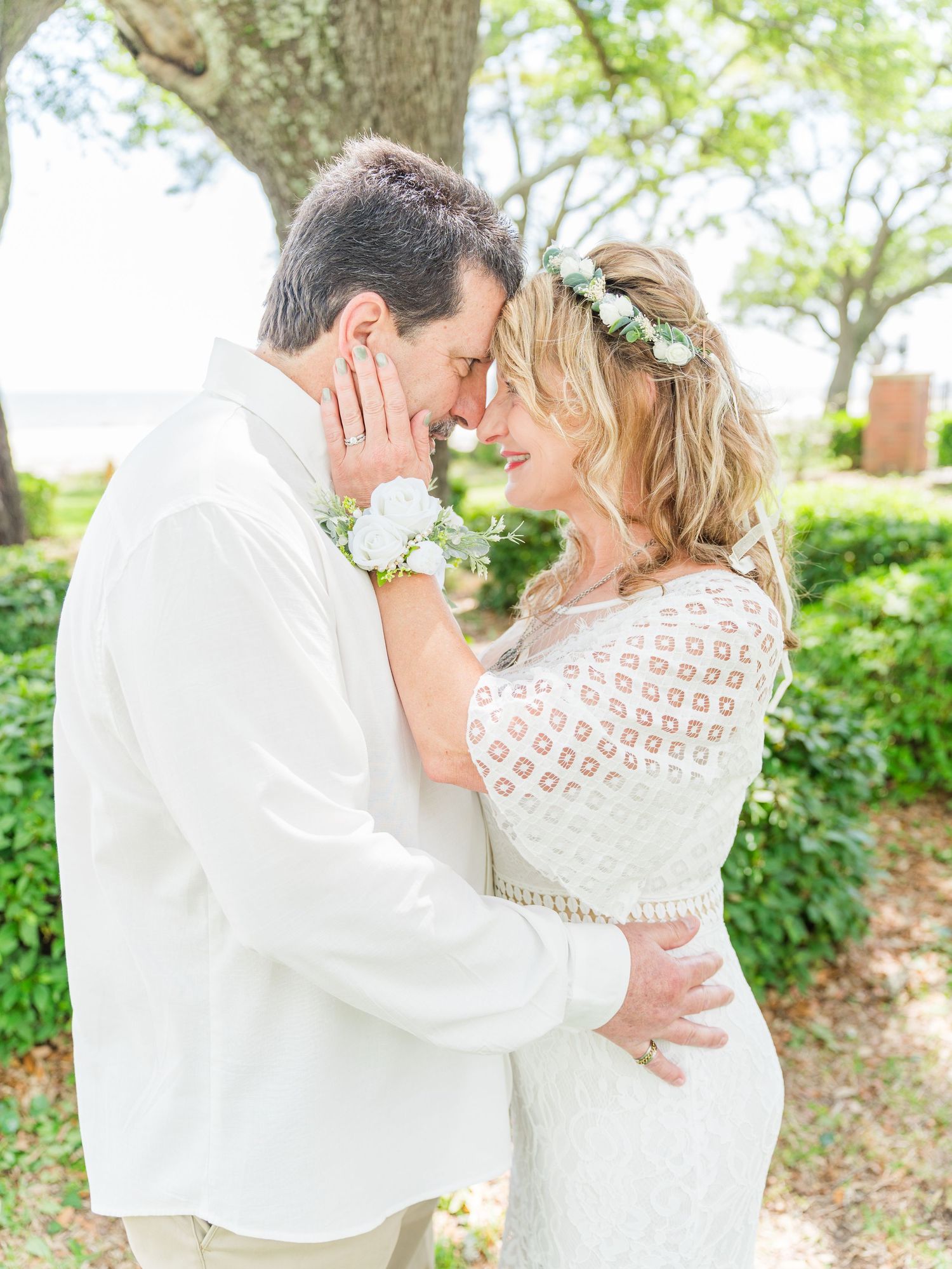 Intimate wedding couple portraits in white attire against lush garden backdrop.