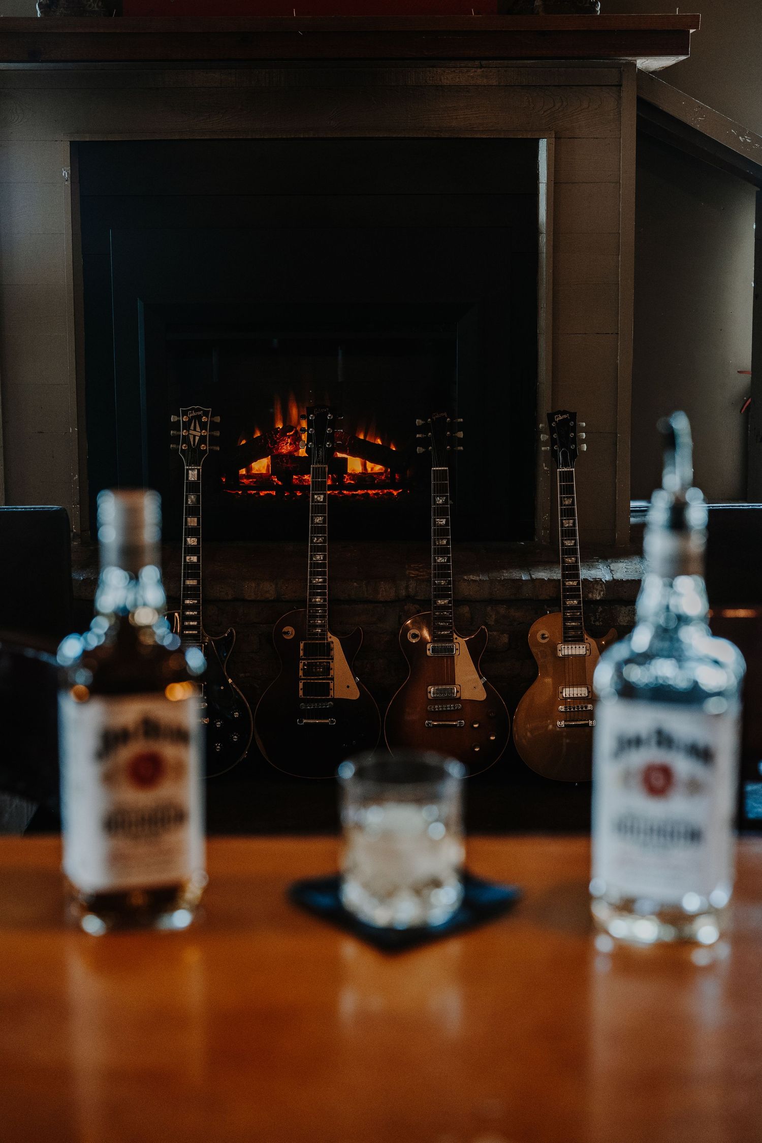 Row of whiskey bottles lined up on a wooden bar counter in dim lighting.