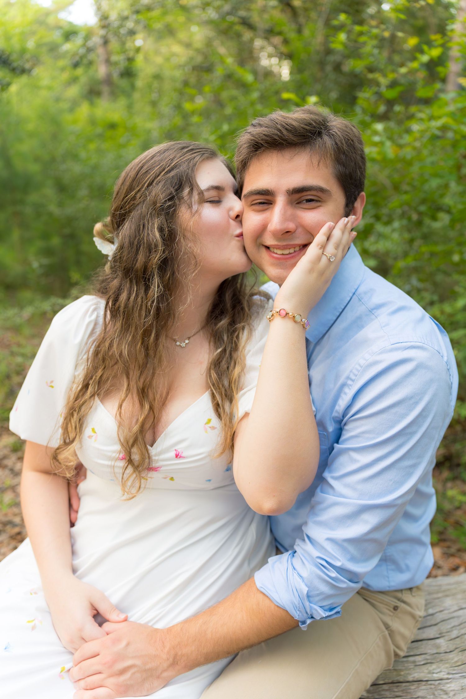 An affectionate couple shares tender moments on a wooden bench in a forest setting.