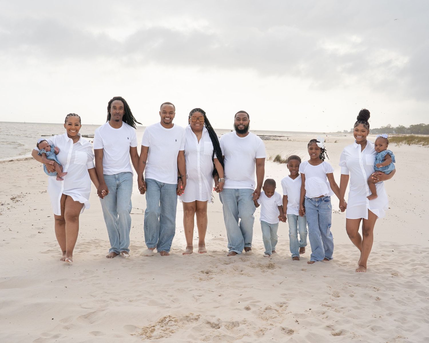 Large family group posed together on beach sand wearing matching casual attire.