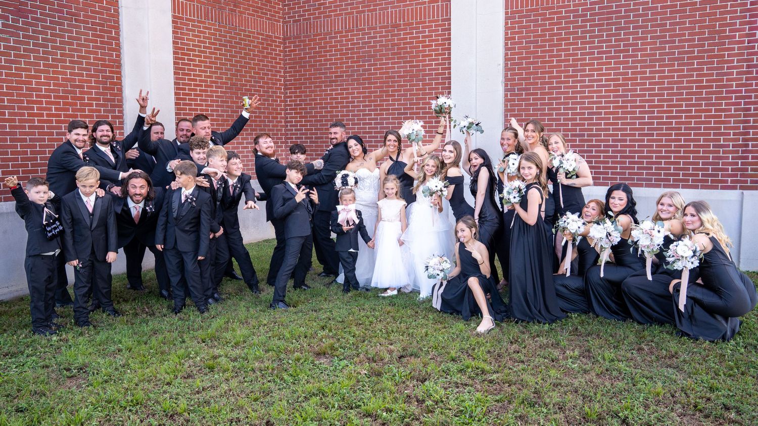 Large group of formally dressed people posed together for a panoramic photo against a brick wall.