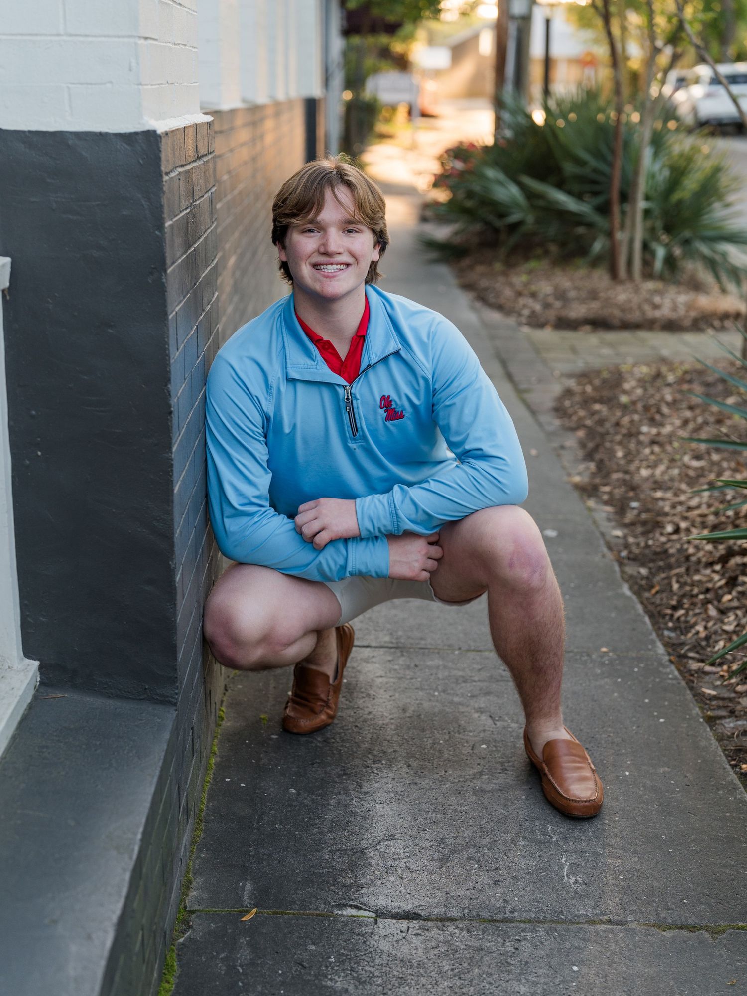 Senior portrait session against dark wall in light blue long-sleeve shirt.