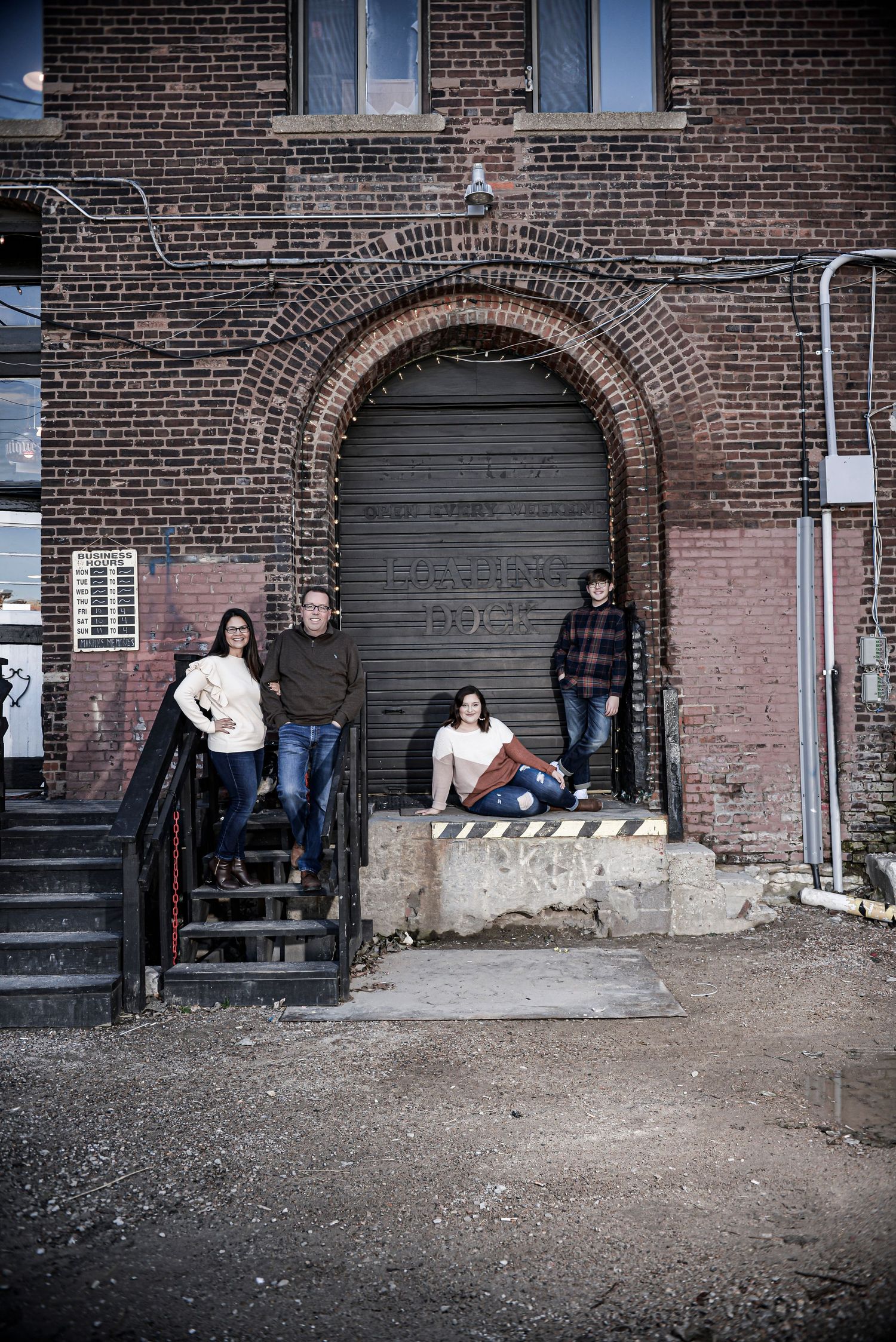 Family portrait of mom, dad, and two adult children by an urban brick building in the West Bottoms of Kansas City
