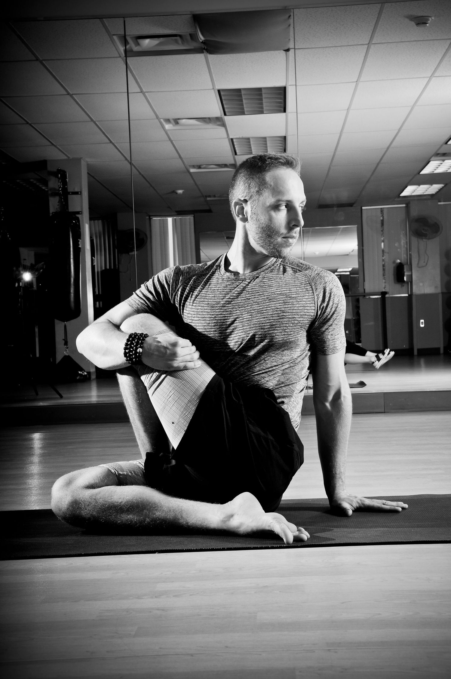 Portrait of yoga instructor in black and white. He is seated and stretching his knee
